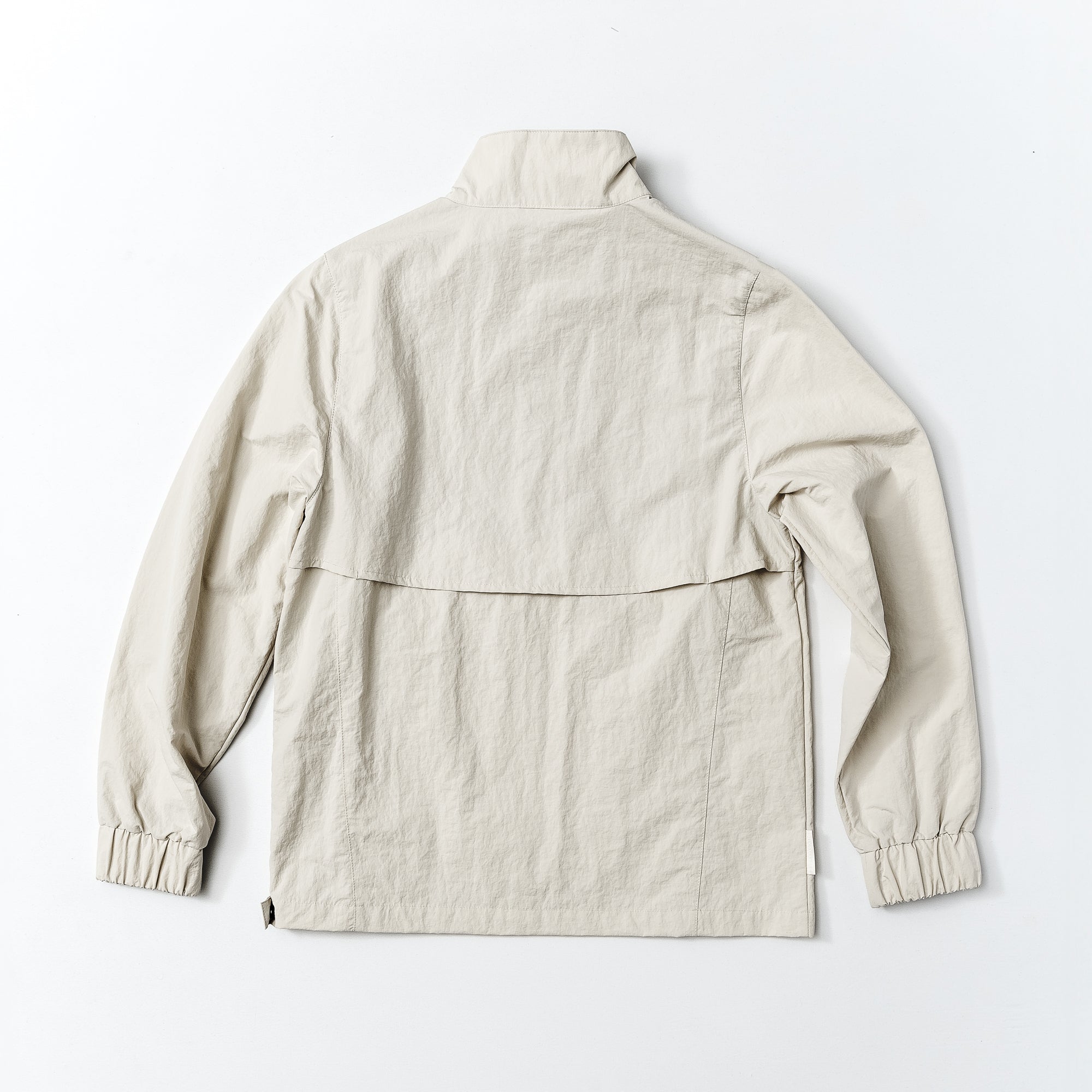 The beardedgoat Womens Sunchase Packable Pullover is shown laid flat, back up, on a white background. It features a collar, vented back yoke, long sleeves with elastic cuffs, and a light beige slightly wrinkled finish.