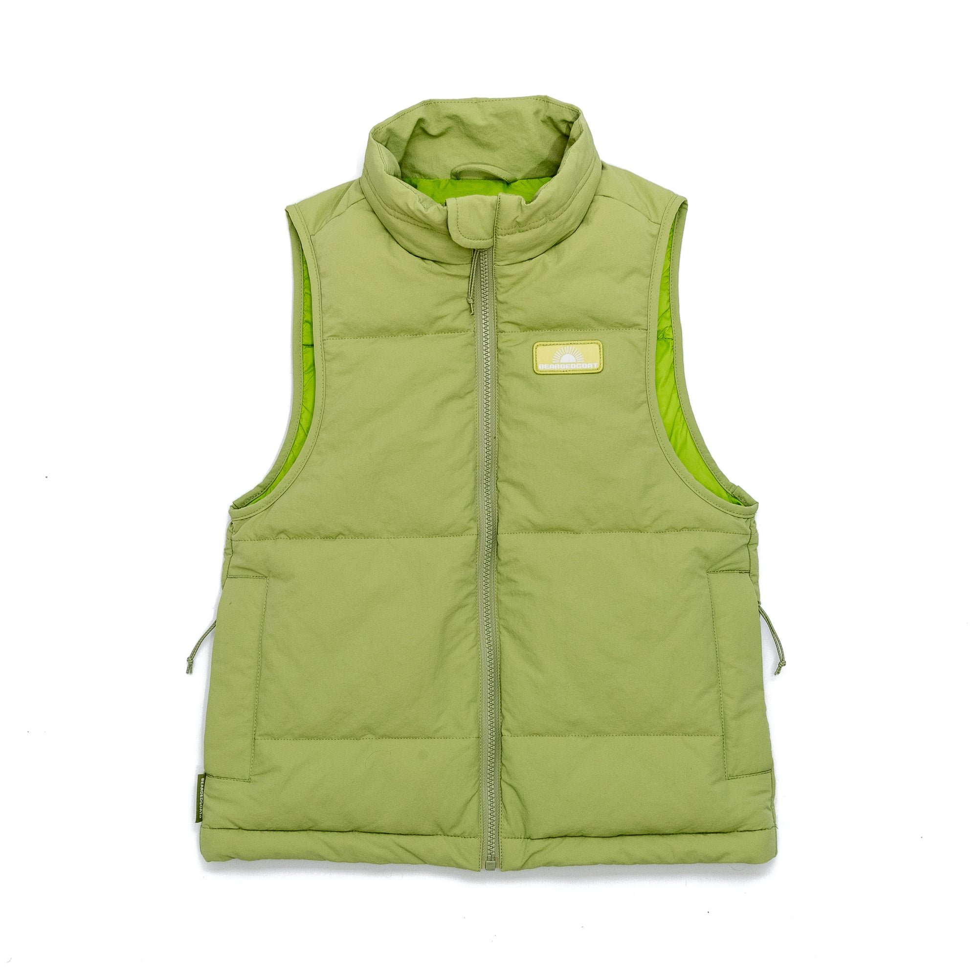 The BEARDEDGOAT Womens Wallowa Puffer Vest - LE is a light green, sleeveless vest with synthetic down insulation, high collar, front zipper, and a small chest logo patch, shown against a white background.