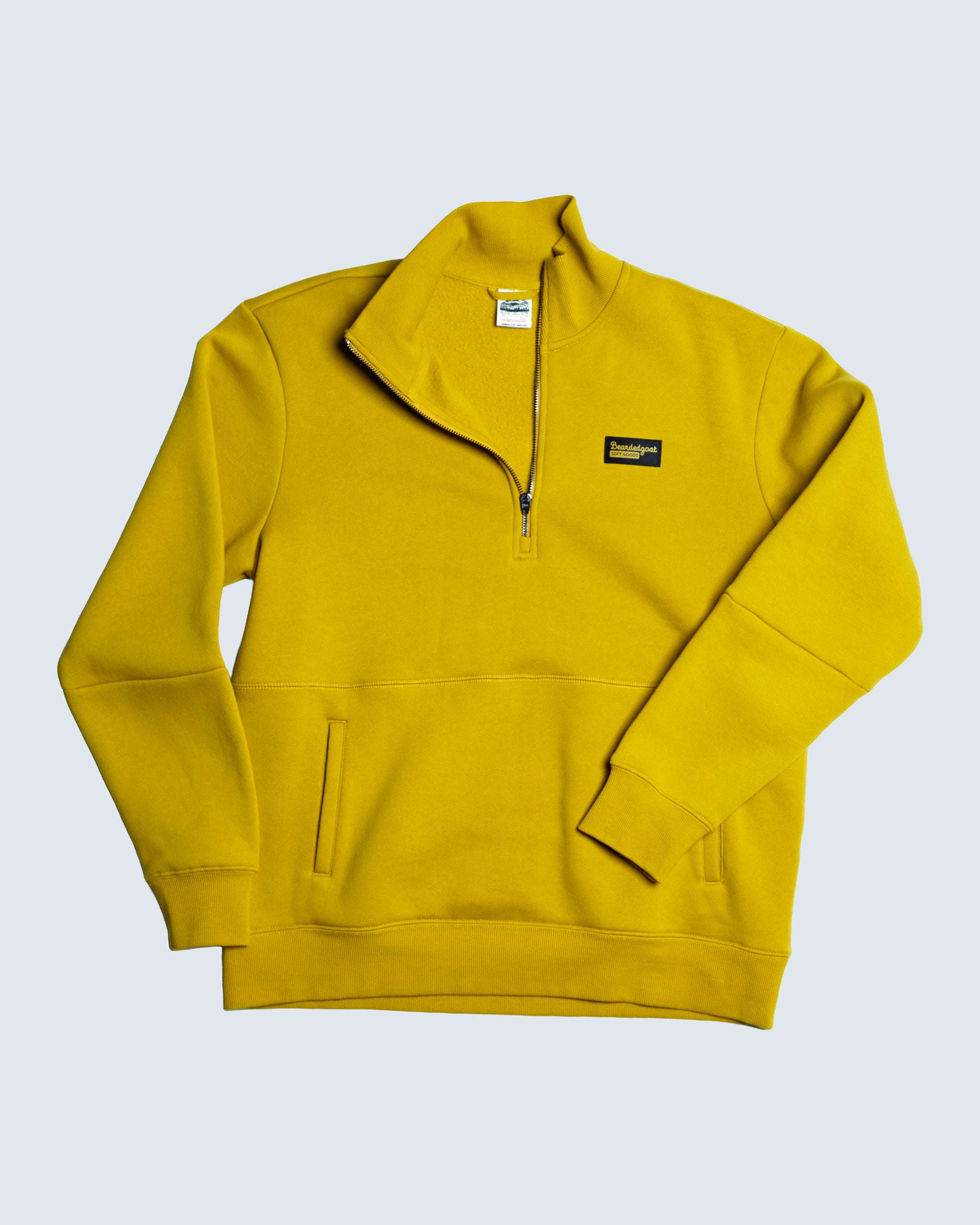 The BEARDEDGOAT NEW — VOID™ Half Zip is a bright yellow premium cotton fleece pullover with a stand-up collar, front pockets, and a small rectangular black chest patch, shown laid flat on a light gray background.