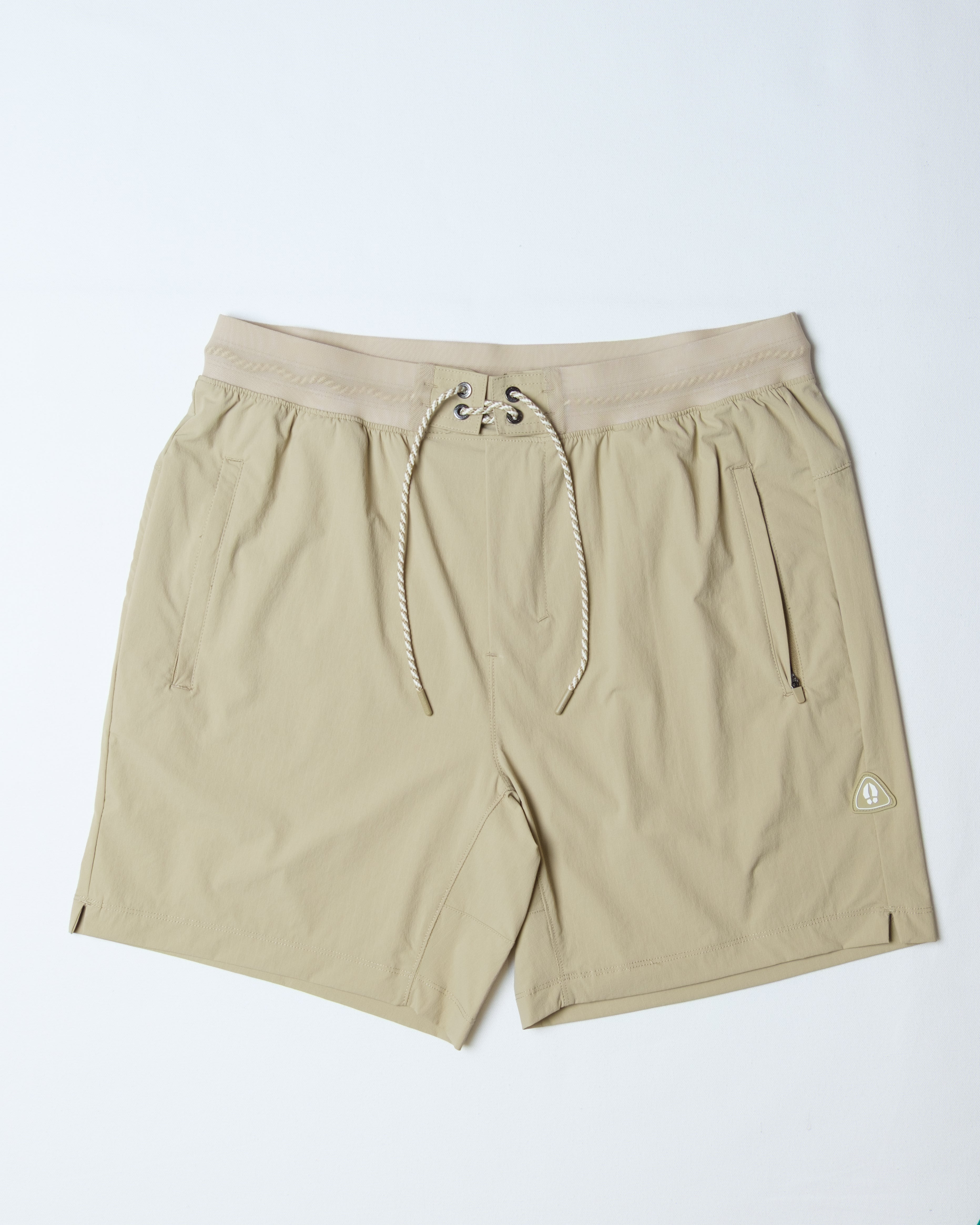 The BEARDEDGOAT Men's Rambler Short in beige features 4-way stretch, a drawstring waist, side pockets, and a small logo on the lower left leg—ideal for trail running. Laid flat on a white background.