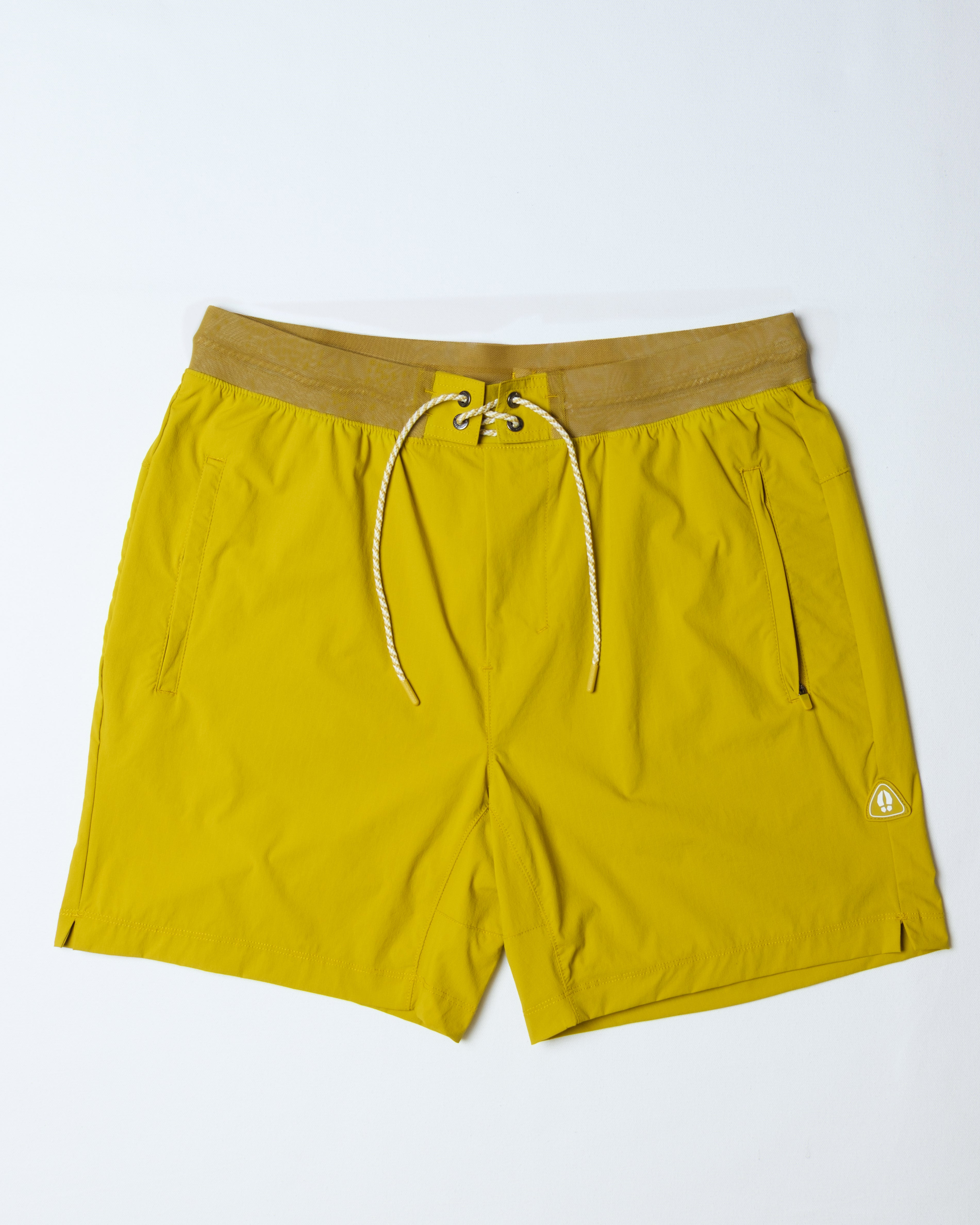 The BEARDEDGOAT Men's Rambler Short in bright yellow features a tan waistband, white drawstring, 4-way stretch fabric, side pockets, and a small logo near the left hem. Shown lying flat on a white background.