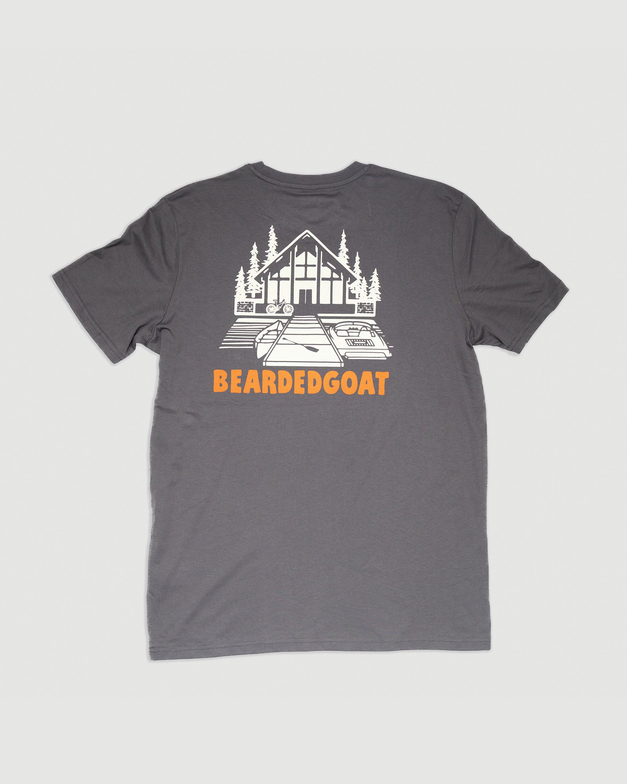 The Weekend Tee - Anthracite by BEARDEDGOAT is a dark gray shirt with a white cabin-and-trees graphic and bold orange BEARDEDGOAT lettering below the image.