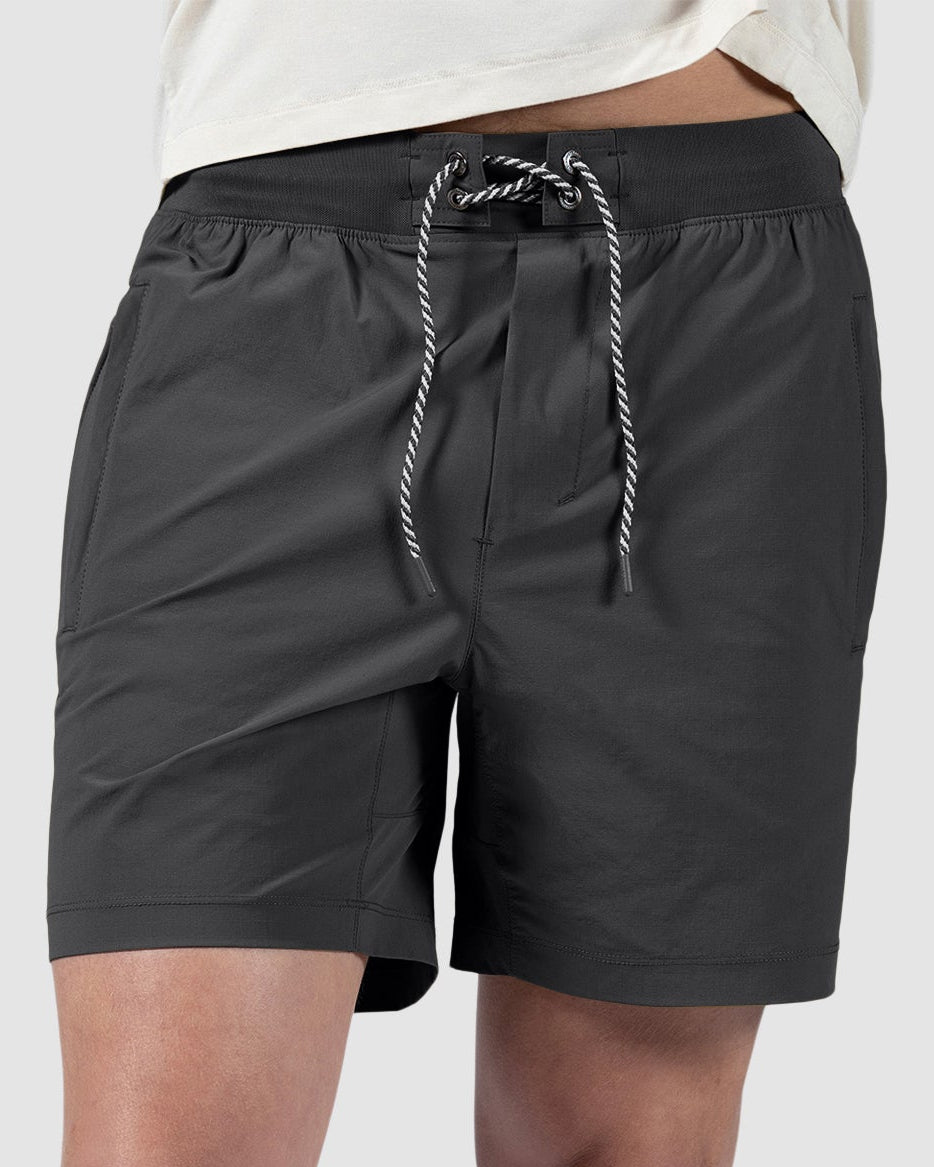 A person in BEARDEDGOAT Mens Rambler Short with 4-way stretch, white sneakers, light socks, and a light t-shirt stands against a gray background—ideal for trail running or everyday wear.