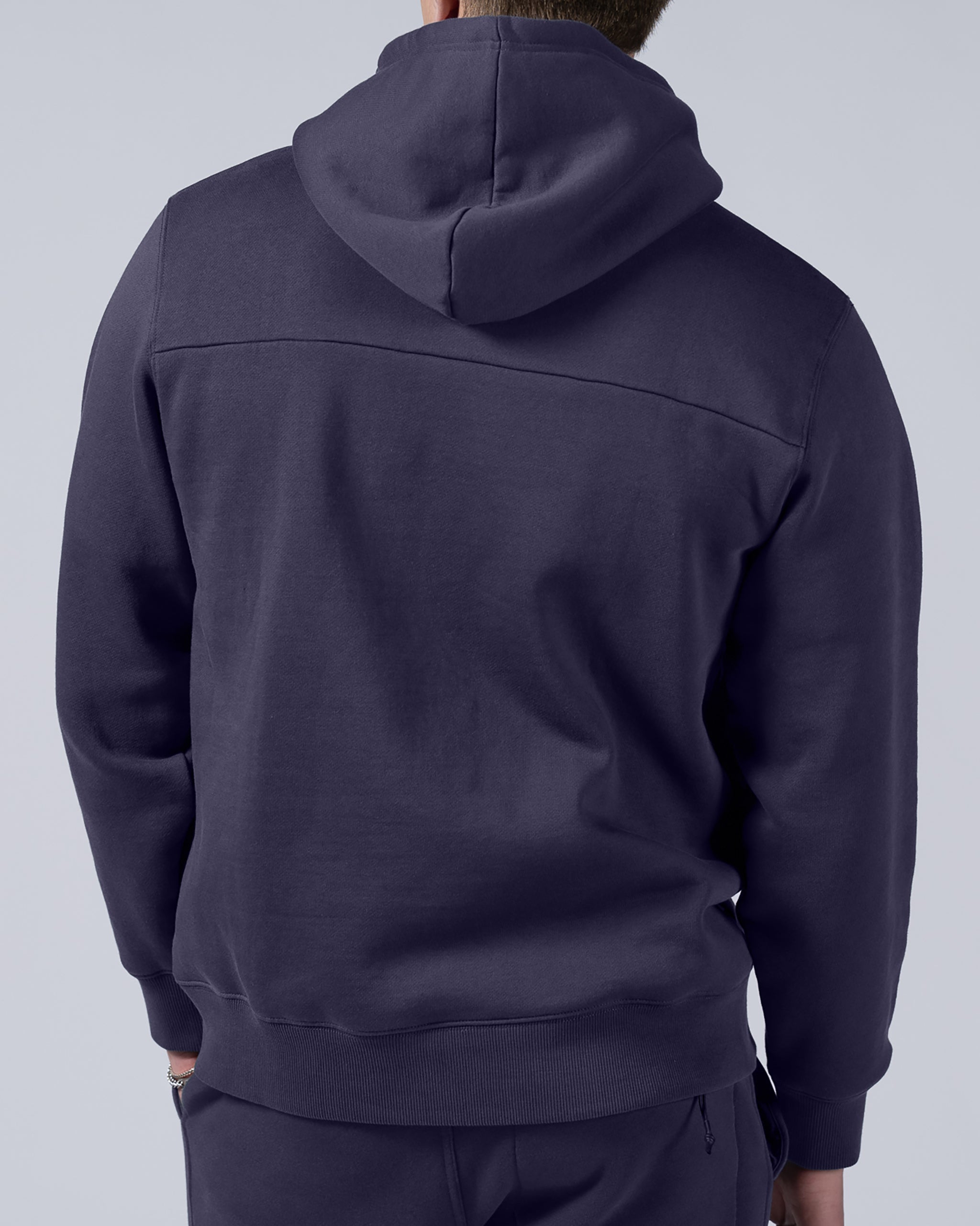 A man is shown from the back wearing the beardedgoat Men's Void Hoodie in dark purple, paired with matching pants, against a plain light gray background. The heavyweight cotton fleece ensures comfort and durability.