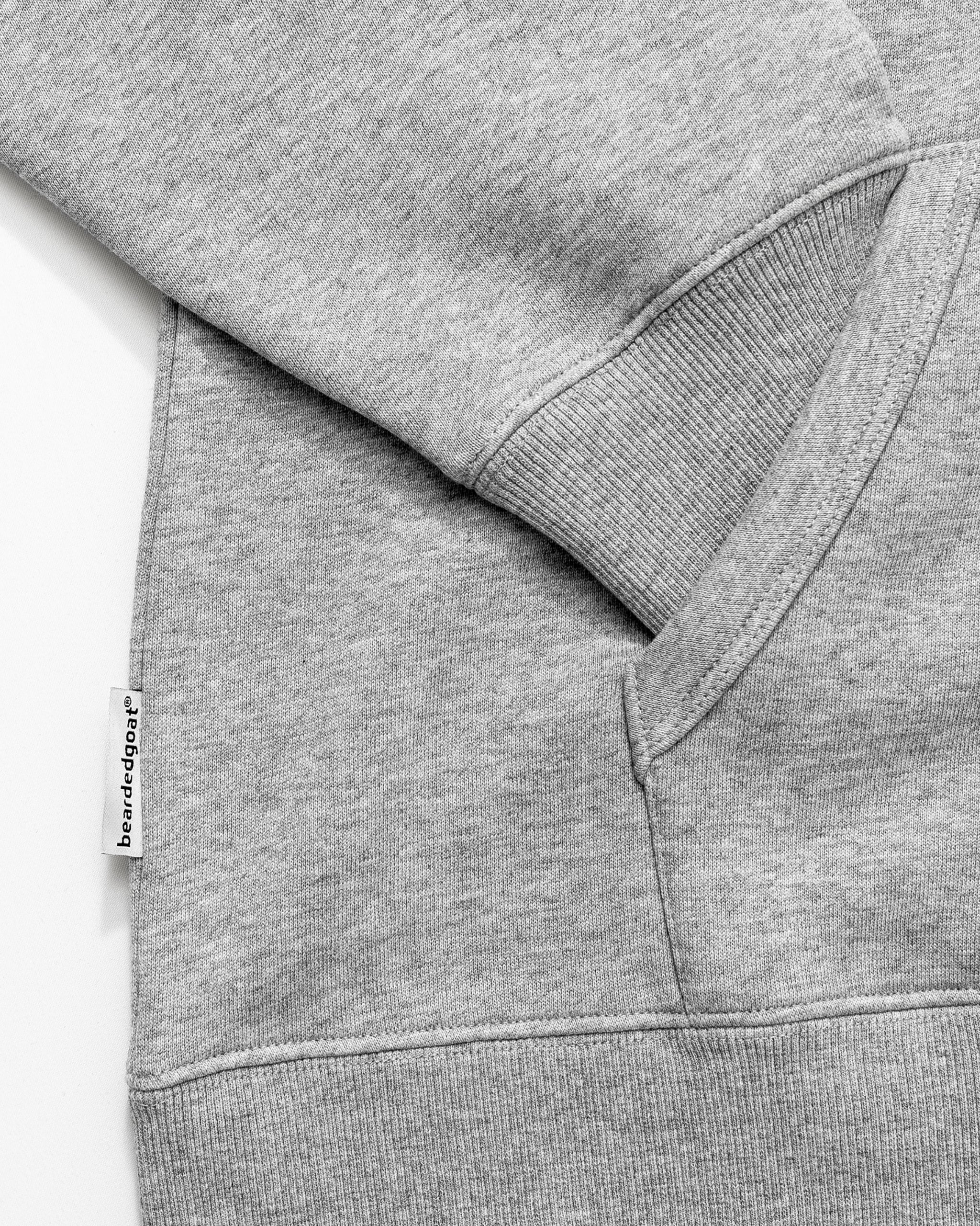 Close-up of the Men's Void Hoodie by beardedgoat in light gray heavyweight cotton, showing a ribbed cuff sleeve, front kangaroo pocket, and a small white "boardapeople" tag, highlighting its durable design and soft textured fabric.