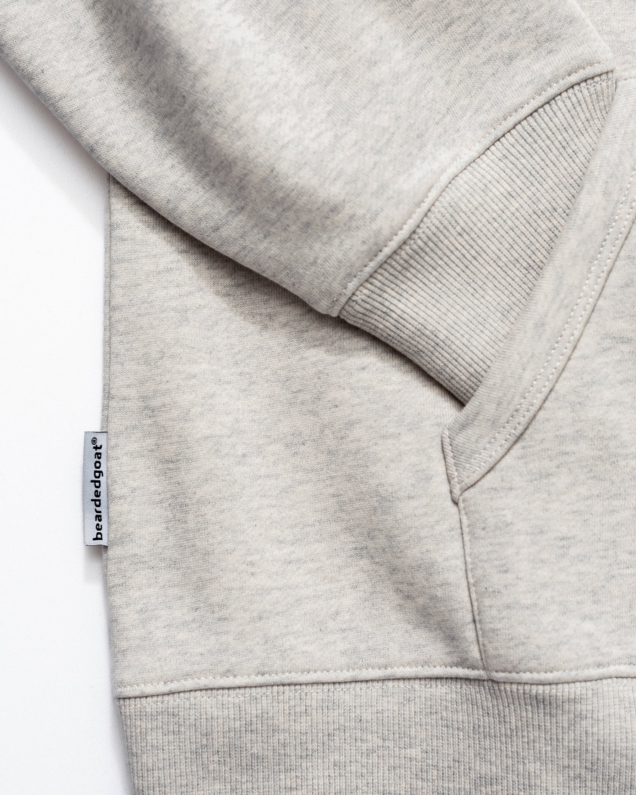 Close-up of the beardedgoat Men's Void Hoodie in light gray, featuring ribbed cuffs, a kangaroo pocket, and a side seam fabric tag, all crafted from heavyweight cotton for lasting durability.
