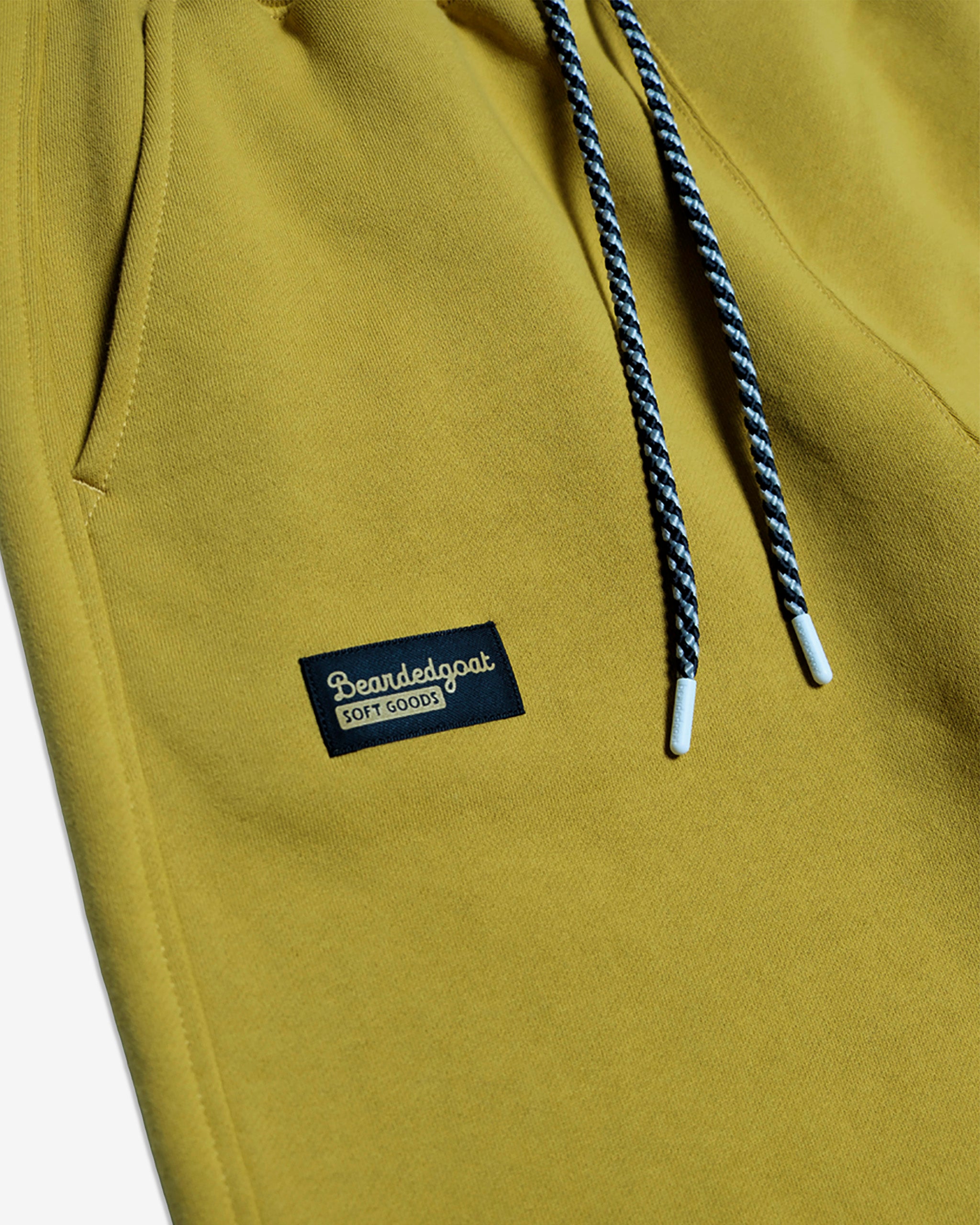 The NEW — Overnight™ Classic Jogger by BEARDEDGOAT features yellow heavyweight cotton fleece, a black and white drawstring, and a black rectangular BEARDEDGOAT SOFT GOODS patch near the pocket for a soft, comfortable feel.