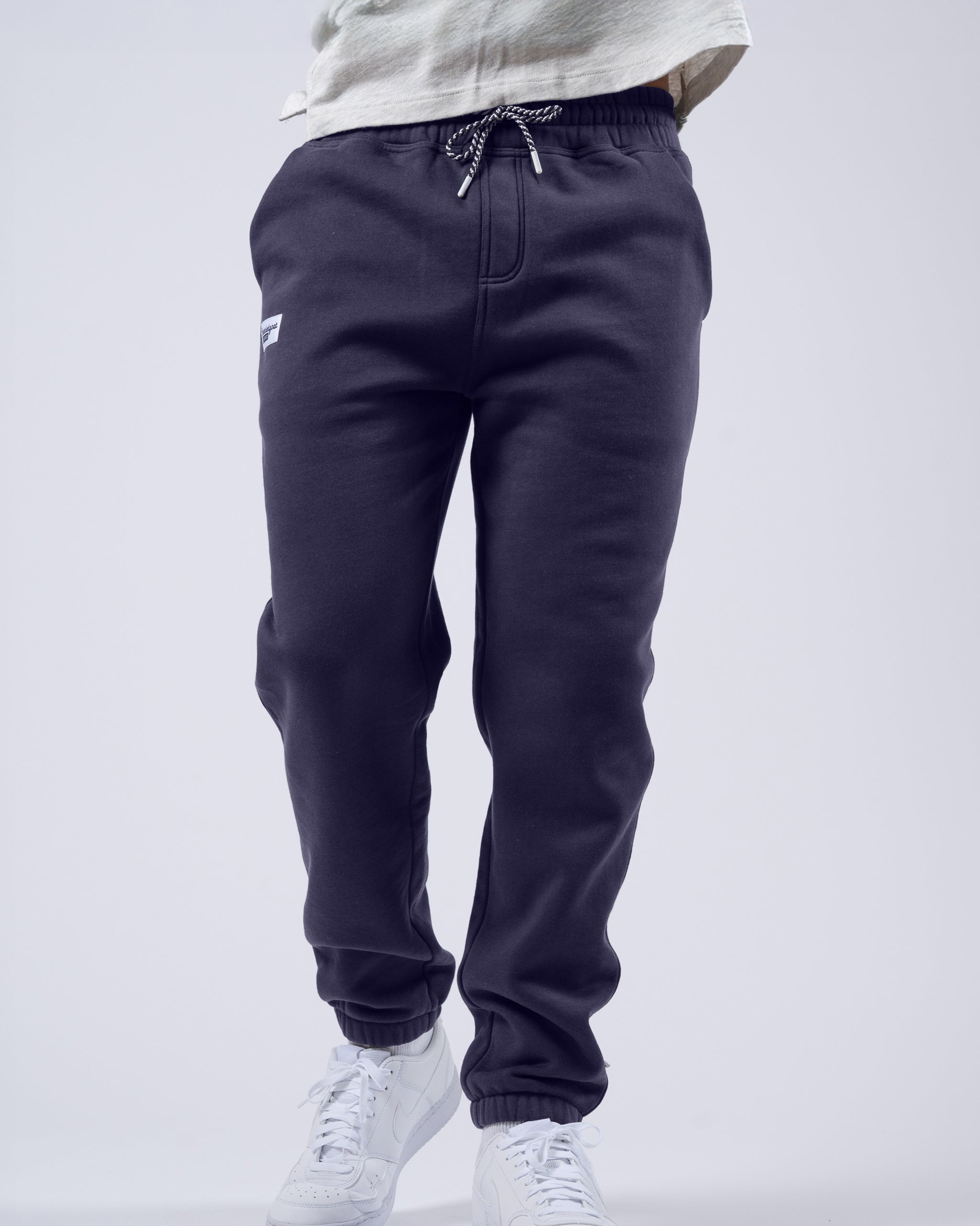 A person wearing beardedgoat Men's Void Sweatpants with a drawstring waist, zipper back pocket, and white sneakers stands against a plain light background. Only the lower body is visible.