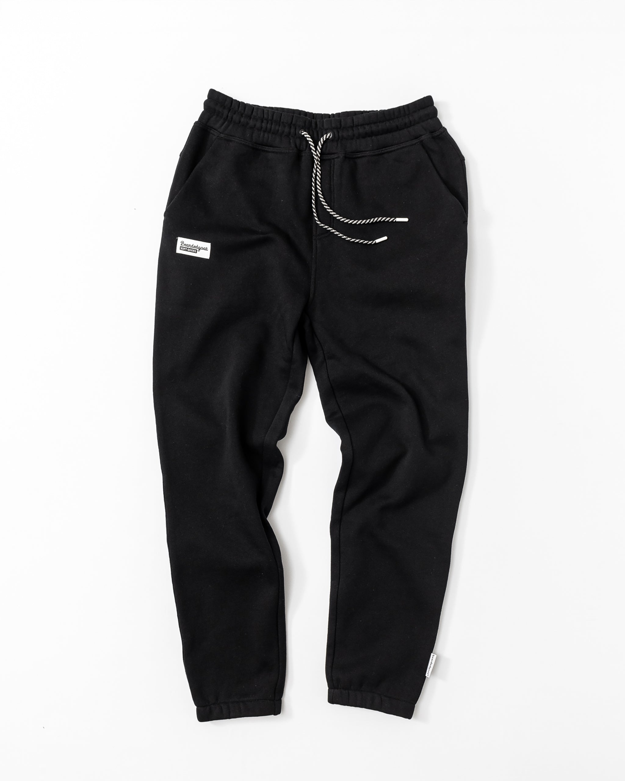 The Men's Void Sweatpants by beardedgoat feature an elastic waistband, white drawstring, small white patch on the left hip, durable design, and a zipper back pocket, shown laid flat on a white background.