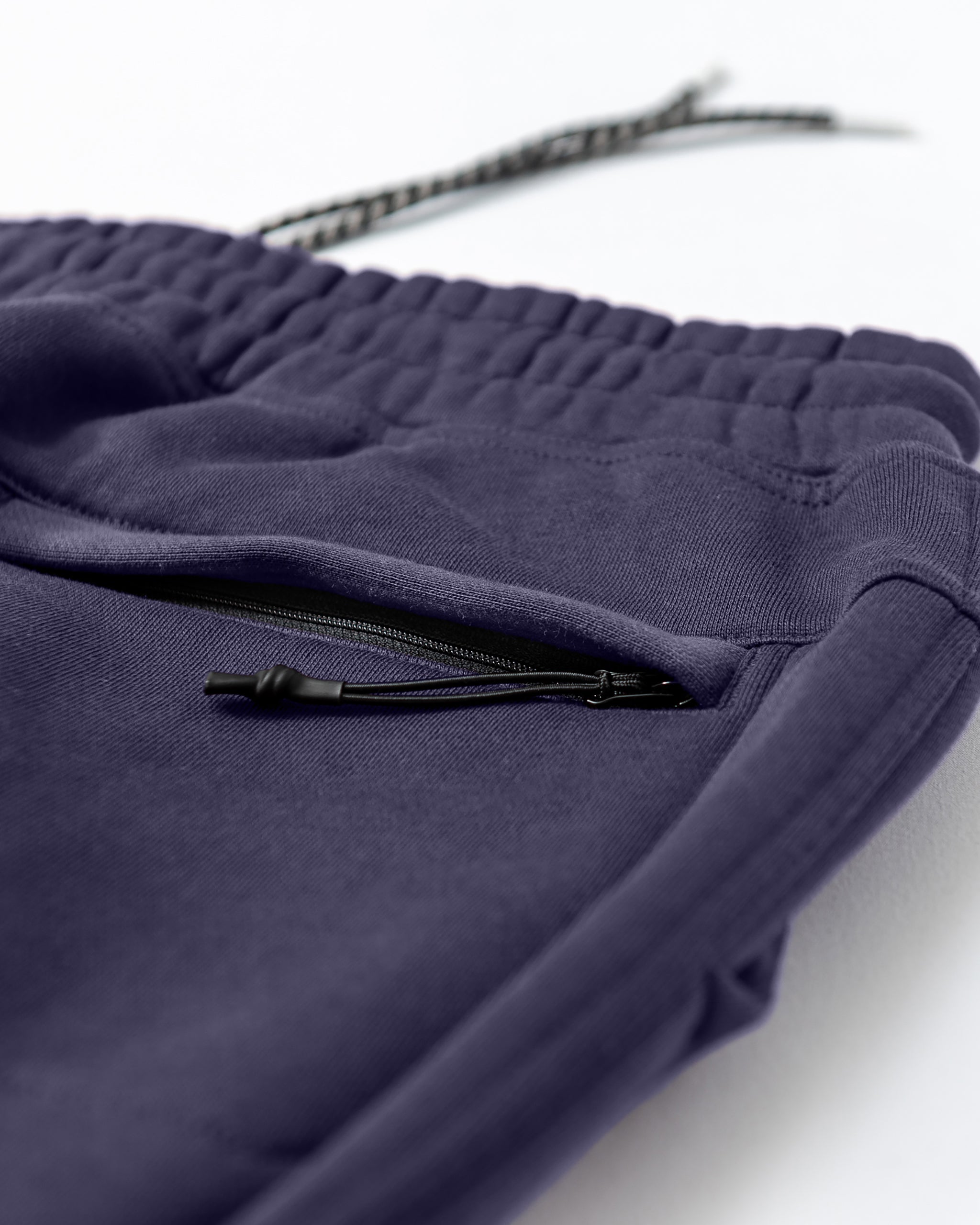 Close-up of Men's Void Sweatpants by beardedgoat in deep purple, featuring an elastic waistband, zippered side pocket, and partially visible drawstring—crafted for durability and lasting comfort.