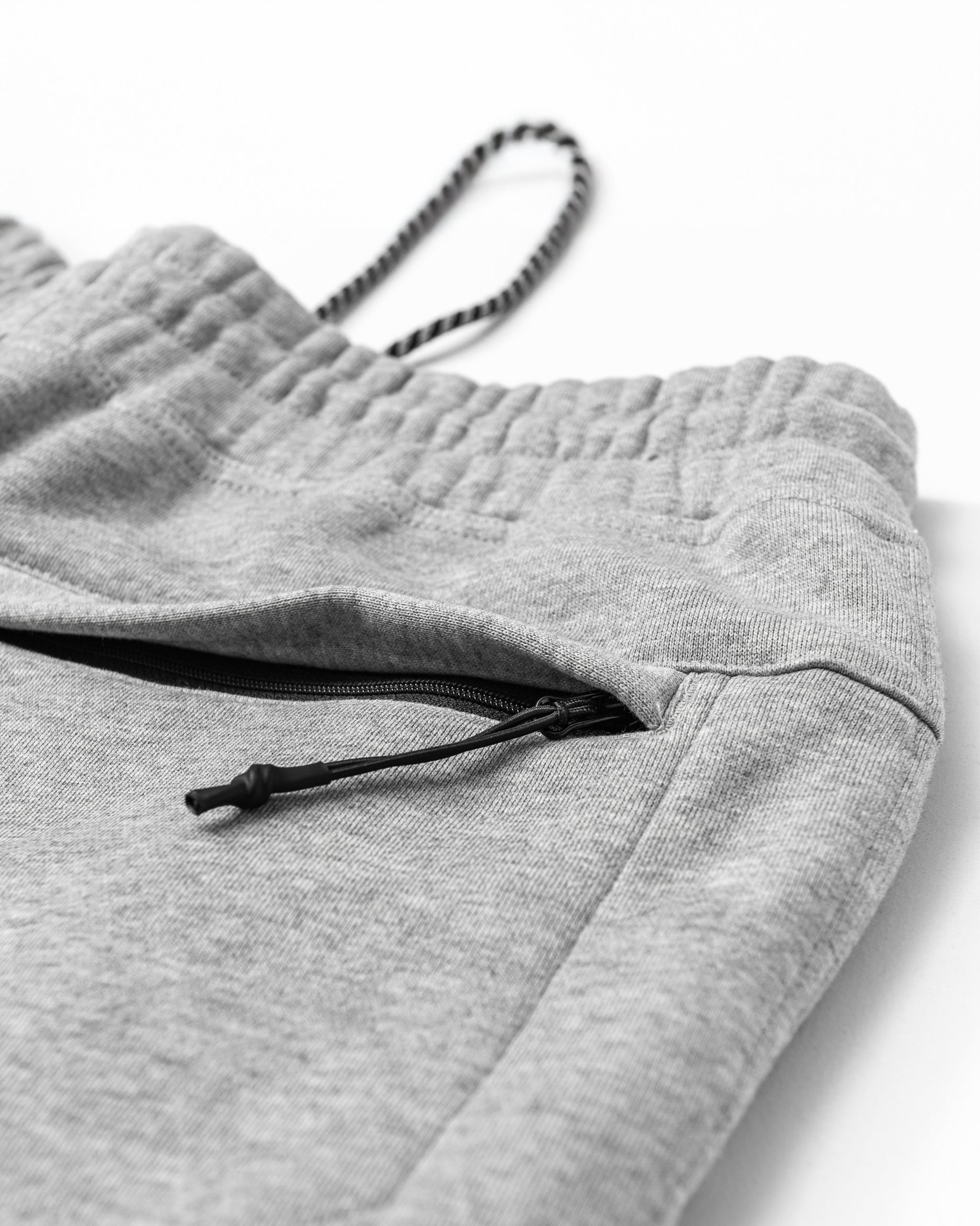 Close-up of beardedgoat Men's Void Sweatpants in light gray, featuring an elastic waistband, black drawstring, and a partially open side pocket with a black zipper. The soft fabric ensures comfort and durability.