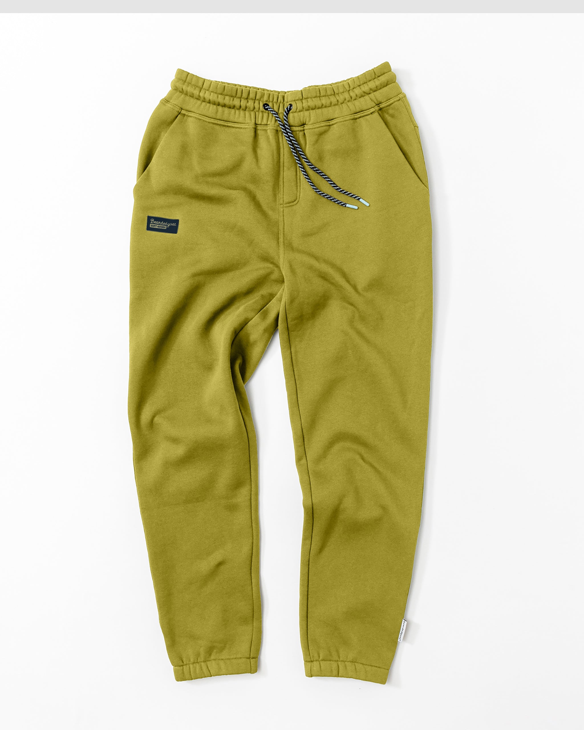 A pair of olive green beardedgoat VOID™ Sweatpants with an elastic waistband, blue and white drawstring, side pockets, and a black patch on the left thigh are laid flat on a white background.