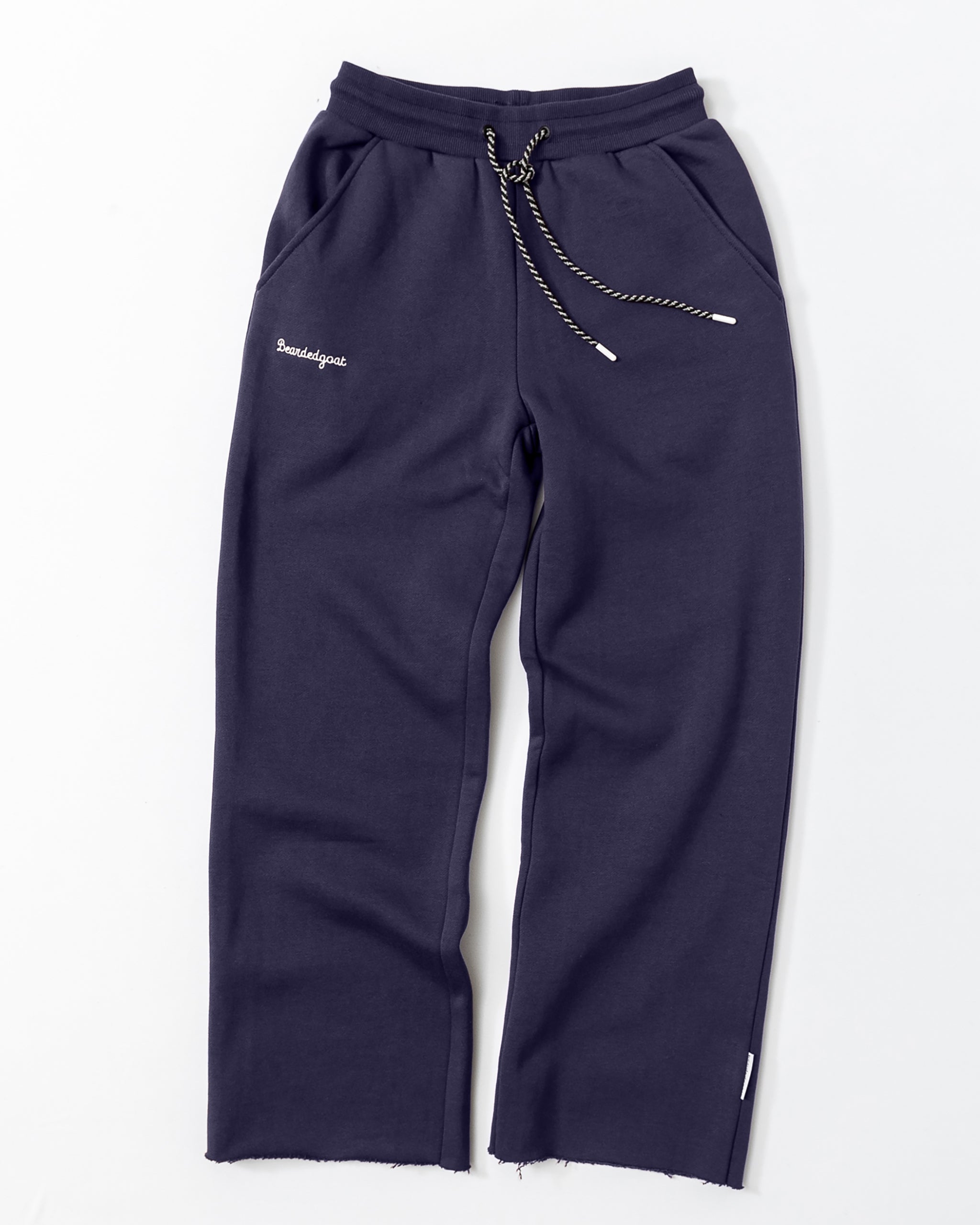 The beardedgoat Women’s Overnight Sweatpant features heavyweight dark blue cotton fleece, an elastic waistband with black-and-white drawstring, front pockets, raw hems, and “Paradigme” white embroidery on the left pocket.