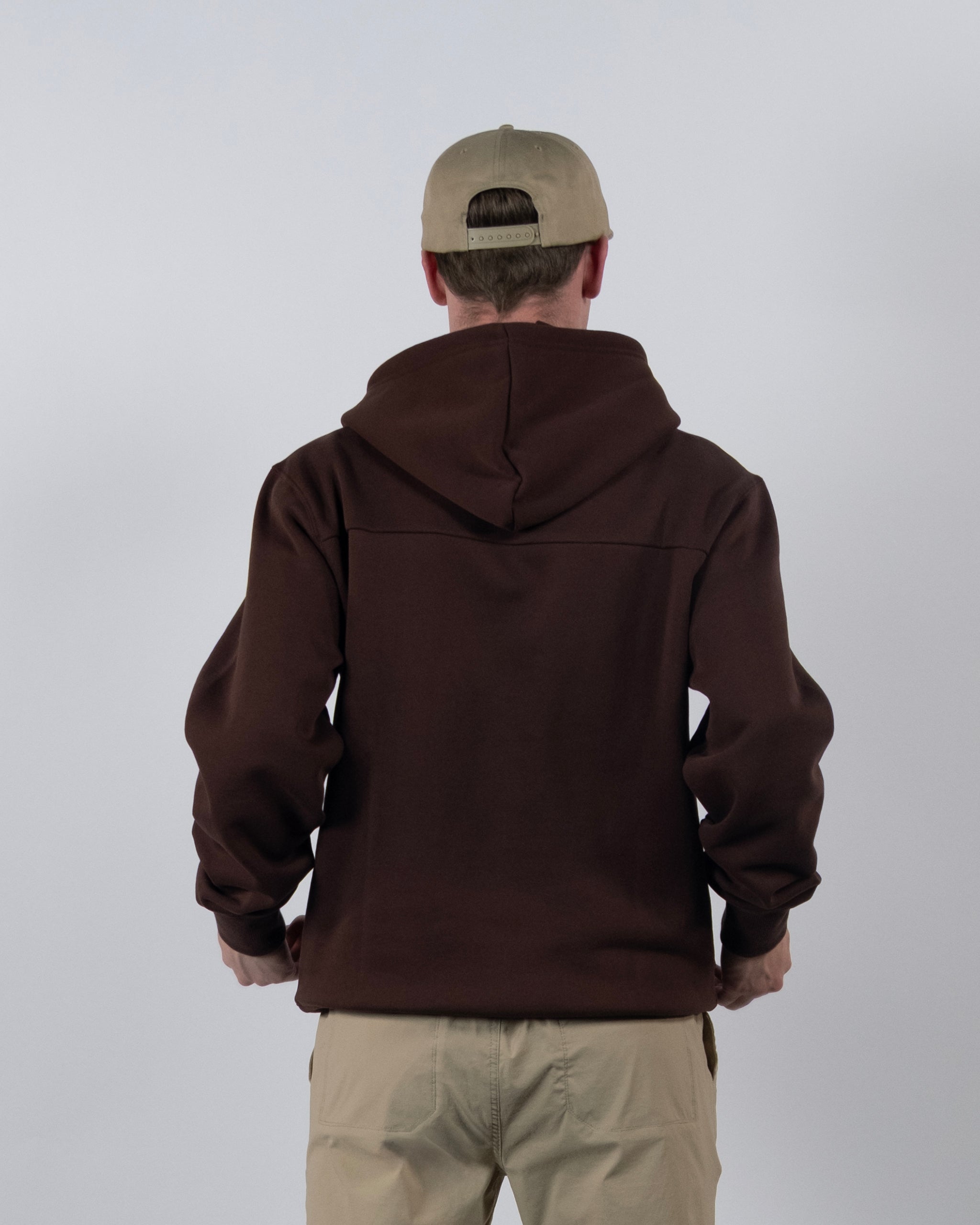 A person in a light beige cap, beige pants, and the beardedgoat The VOID™ Hoodie stands with their back to the camera against a plain, light-colored background.