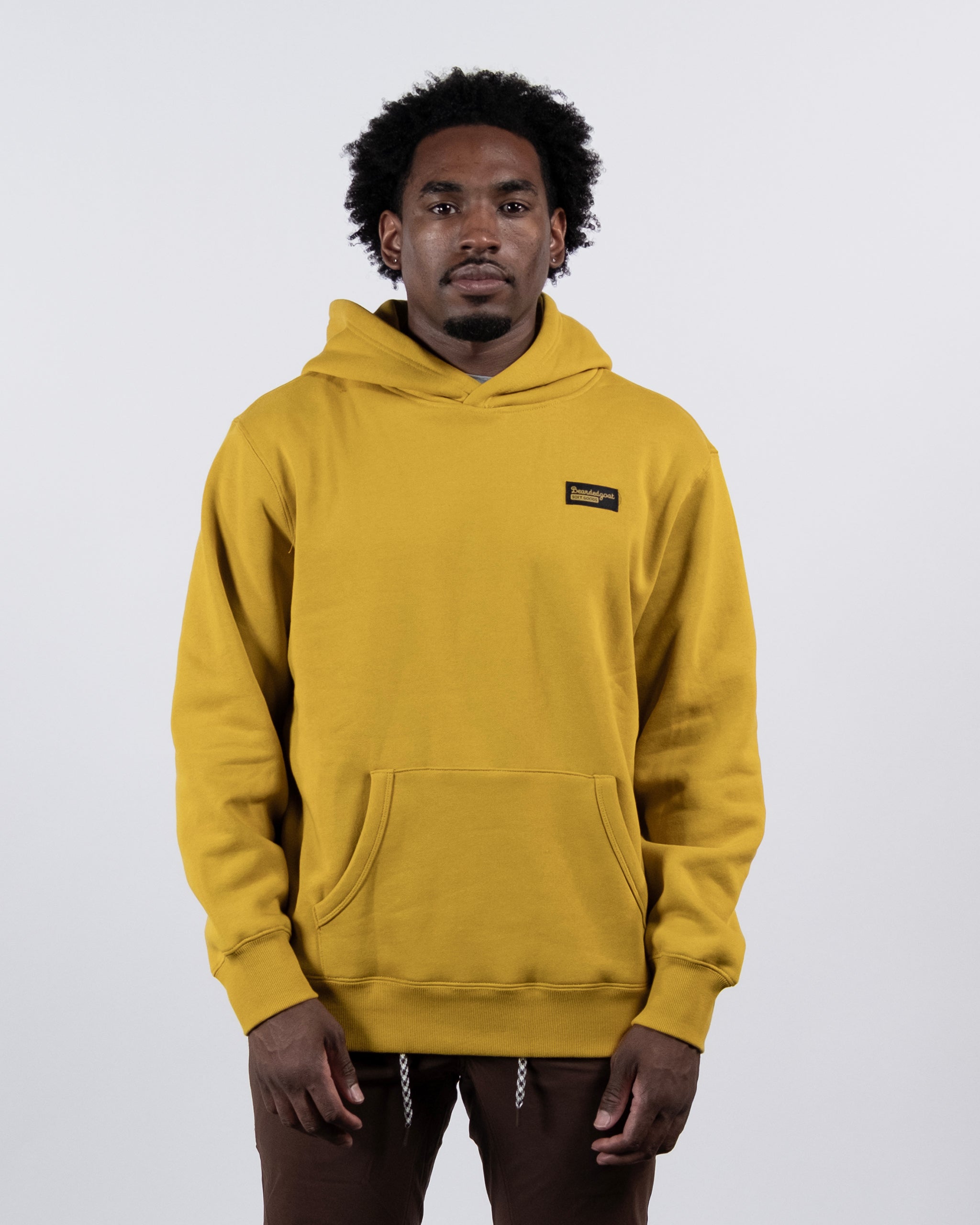A man with short curly hair wears the VOID™ Hoodie by beardedgoat, made from heavyweight cotton fleece with a front pocket and small rectangular logo, standing against a plain light gray background.