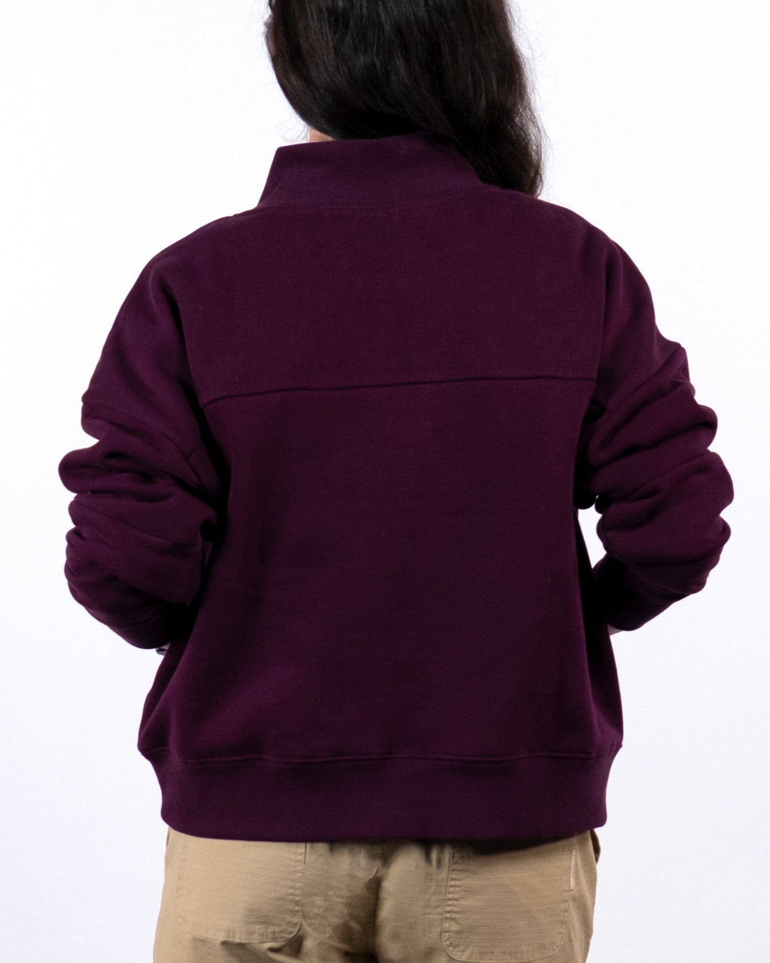 Seen from behind, a person with long dark hair wears the BEARDEDGOAT NEW — Overnight™ Half Zip heavyweight fleece sweatshirt in dark purple and light tan shorts, set against a plain white background.