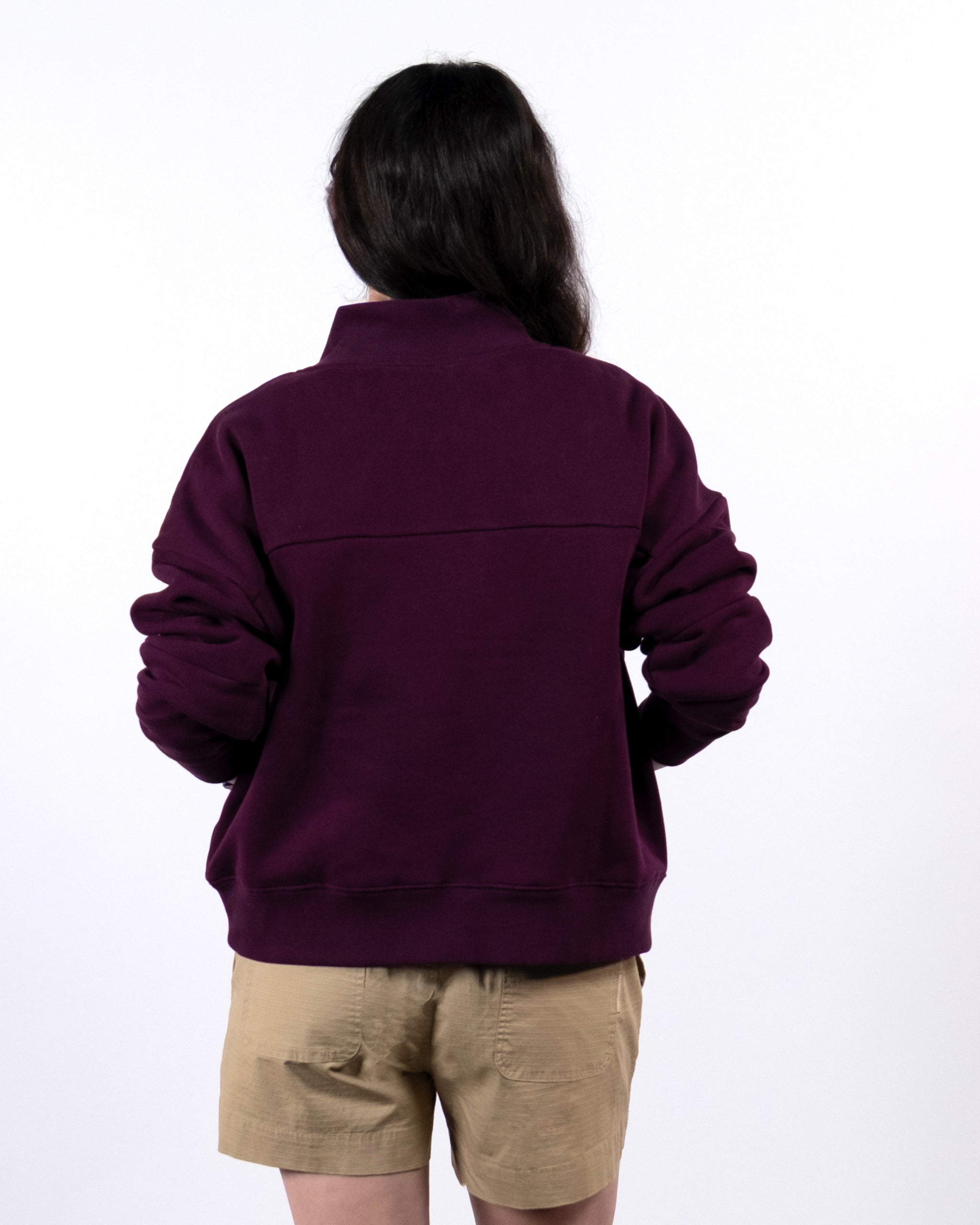 Seen from behind, a person with long dark hair wears the BEARDEDGOAT NEW — Overnight™ Half Zip heavyweight fleece sweatshirt in dark purple and light tan shorts, set against a plain white background.