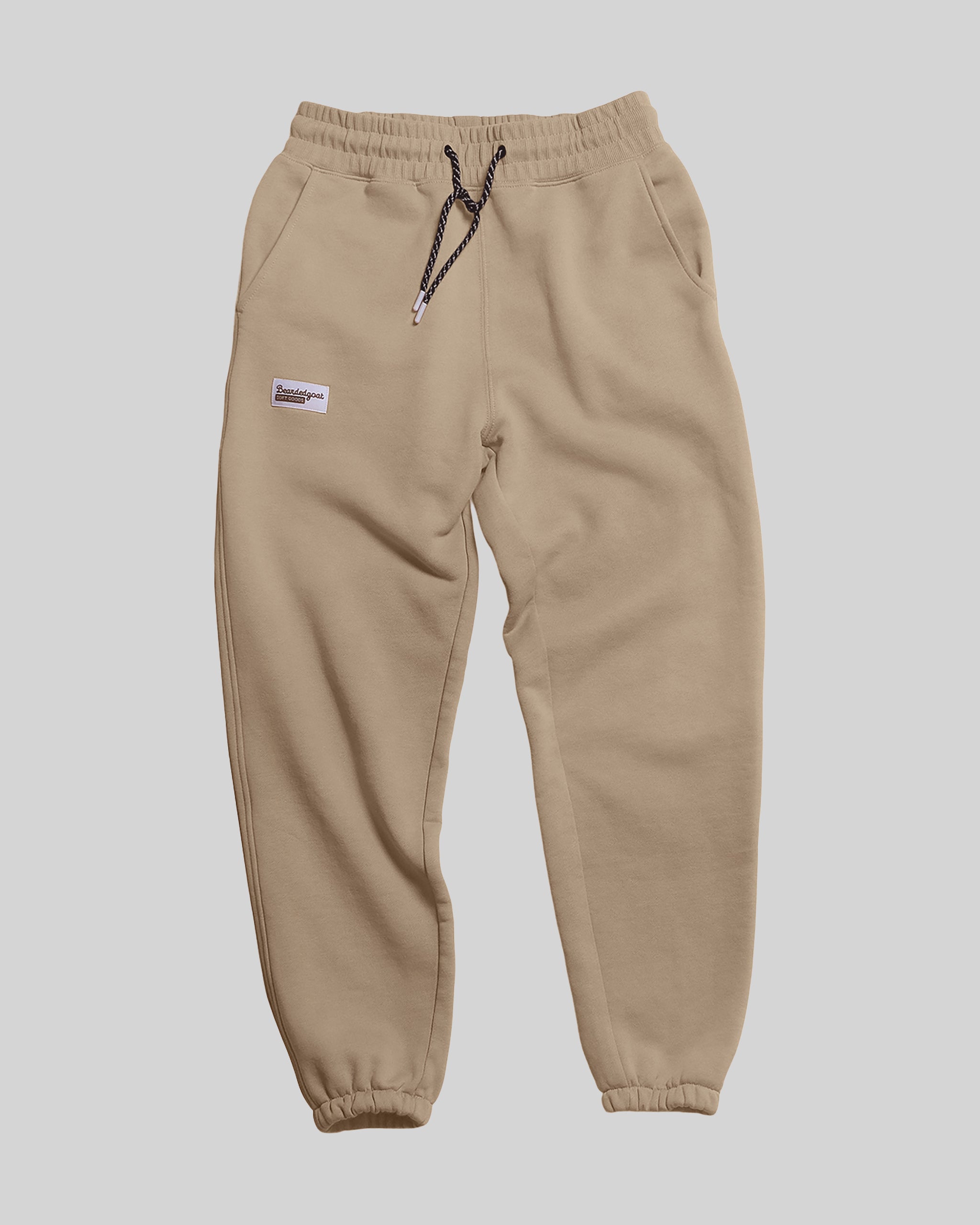The BEARDEDGOAT NEW — Overnight™ Classic Jogger features beige heavyweight cotton fleece, a high-rise elastic waistband with black and white drawstring, side pockets, and a small white patch on the left thigh. Displayed on a plain light background.