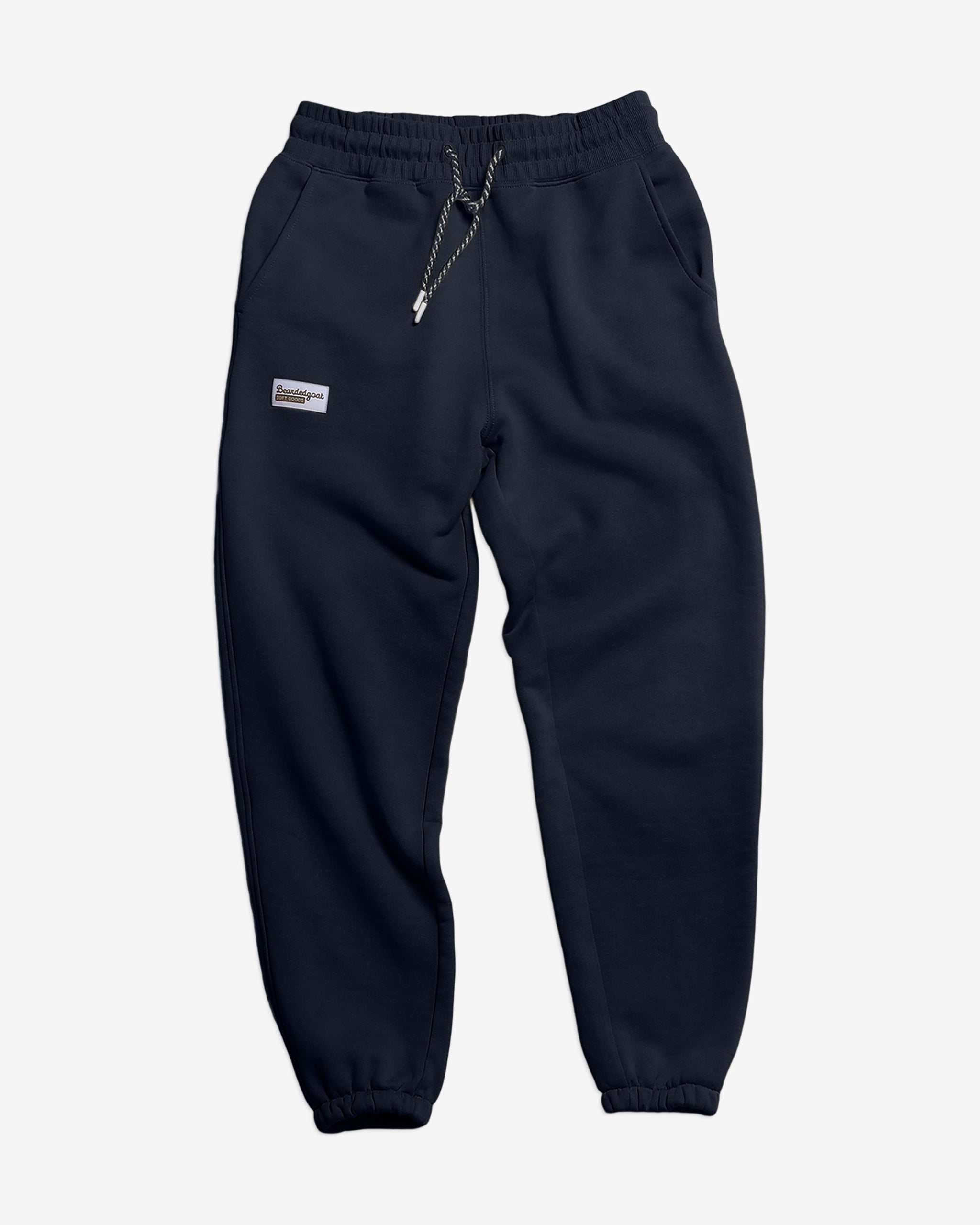 The Women’s Overnight™ Classic Jogger by BEARDEDGOAT features navy blue heavyweight cotton fleece, an elastic high-rise waistband with drawstring, side pockets, and a small rectangular label above the left pocket. Shown on a white background.
