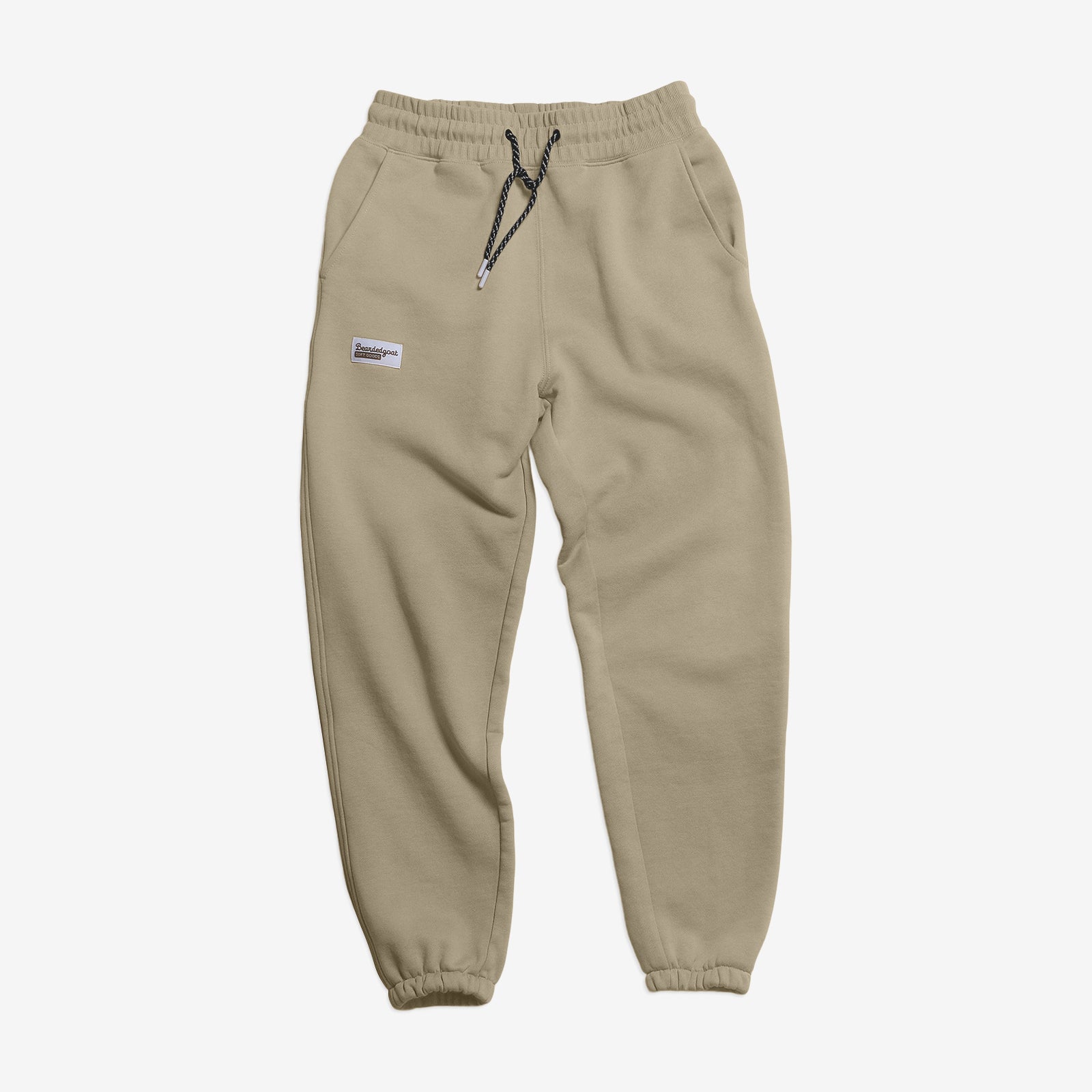The BEARDEDGOAT Women’s Overnight™ Classic Jogger features heavyweight beige cotton fleece, an elastic high-rise waistband with black drawstring, side pockets, elastic cuffs, and a small patch on the left thigh. Shown laid flat on white.