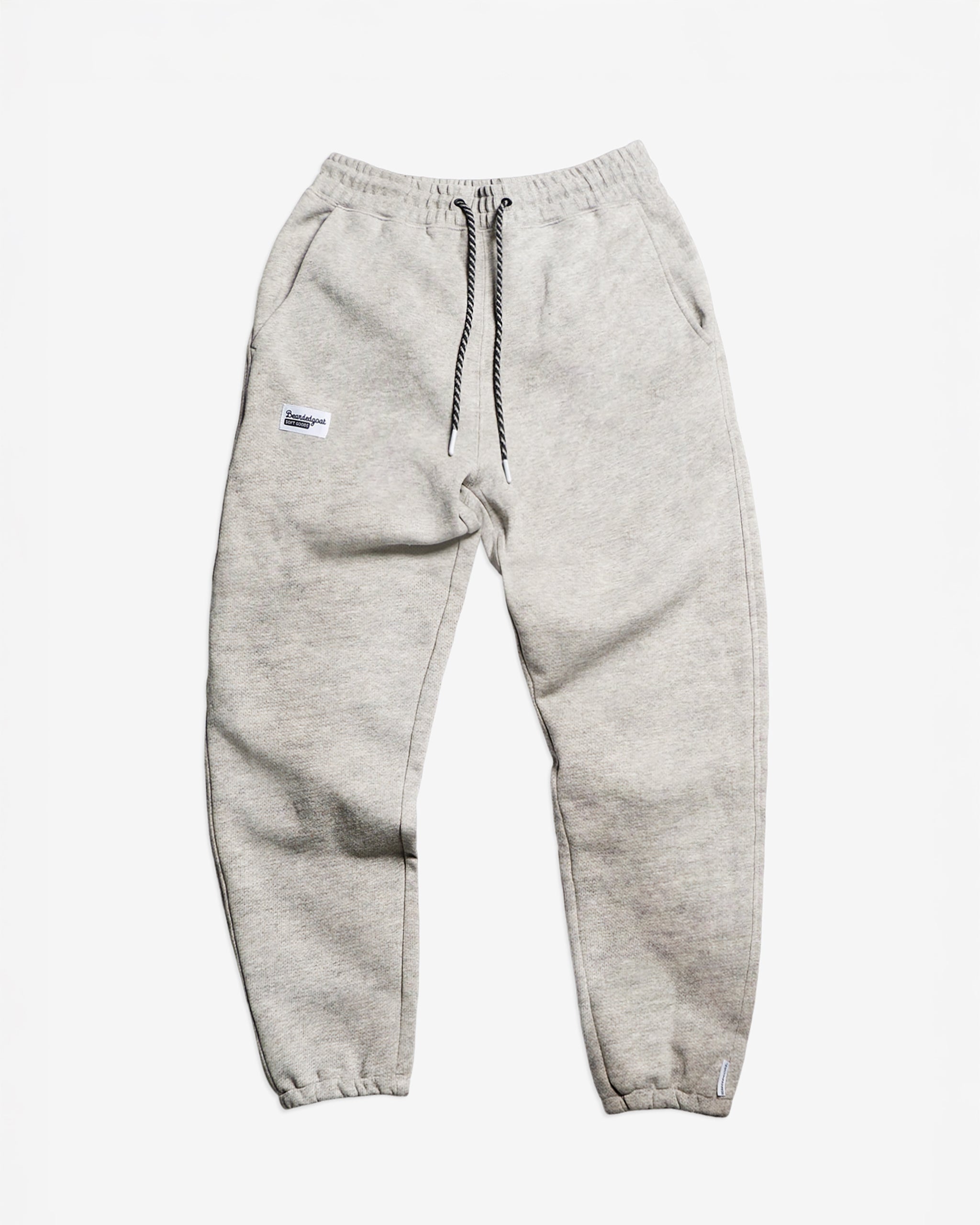 The BEARDEDGOAT Women’s Overnight™ Classic Jogger in Snow Grey features a high-rise waistband, black-and-white drawstring, side pockets, and a white patch on the left leg, crafted from heavyweight cotton fleece.