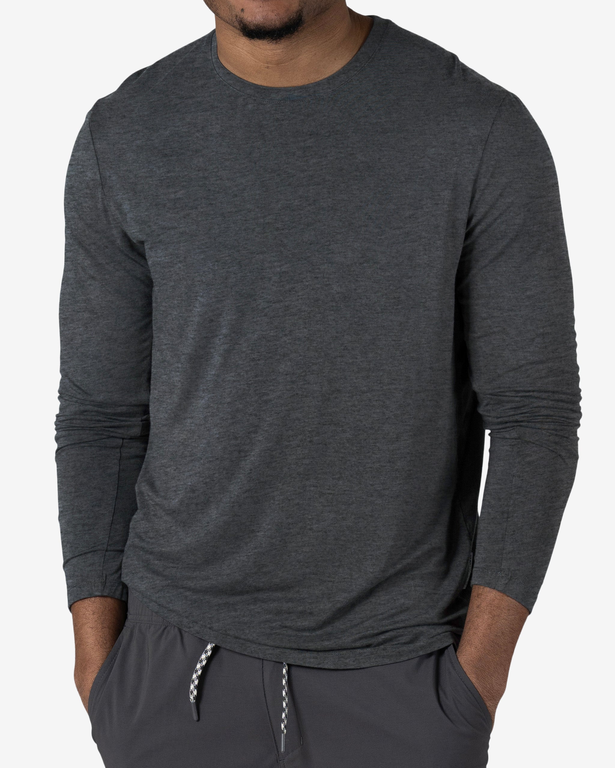 A man stands with his hands in his pockets against a plain white background, wearing the BEARDEDGOAT Men’s EverZen™ Long Sleeve dark gray shirt and gray drawstring pants.