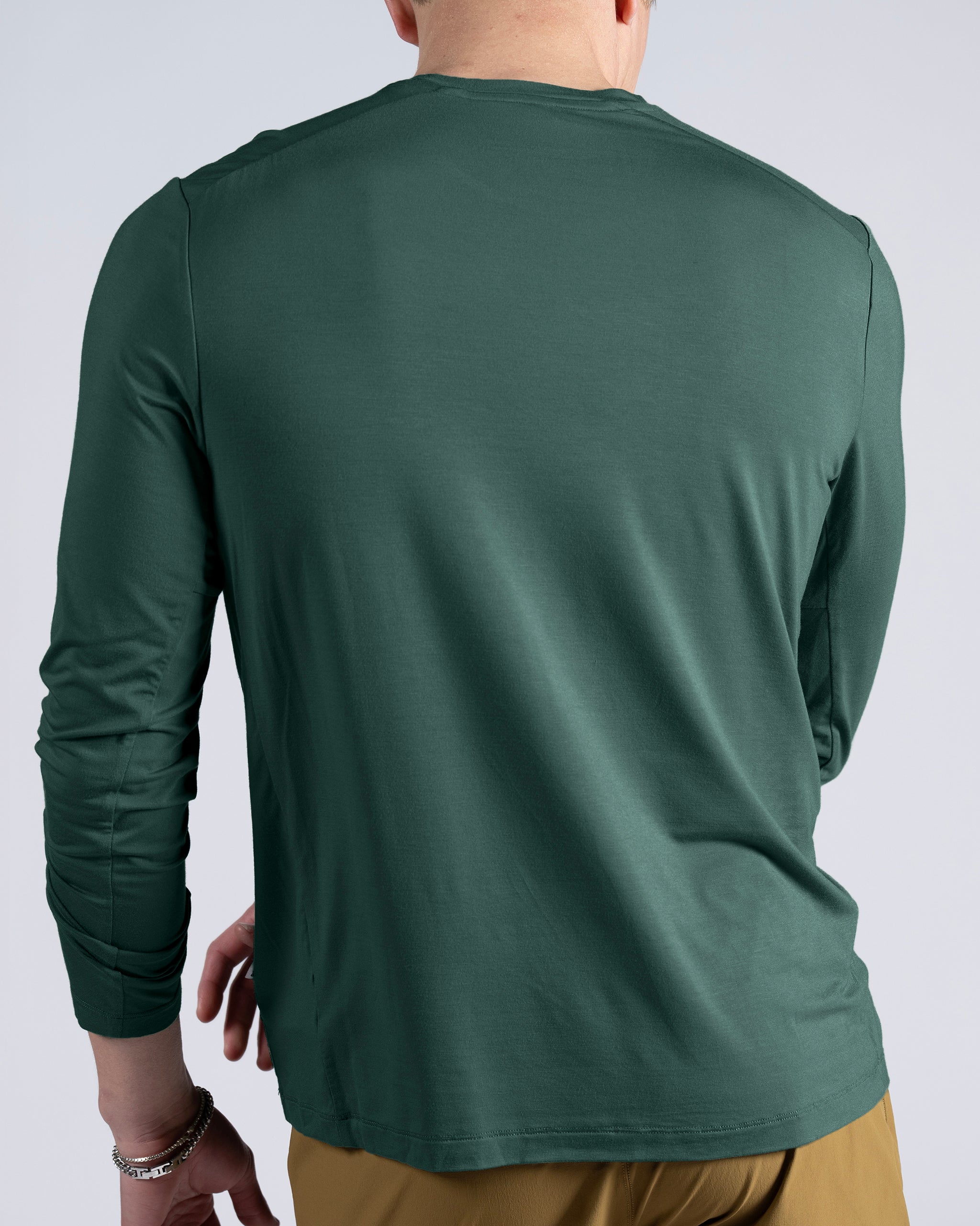 A person wearing a BEARDEDGOAT Men’s EverZen™ Long Sleeve crew neck in dark green and light brown pants is shown from the back against a plain light background.