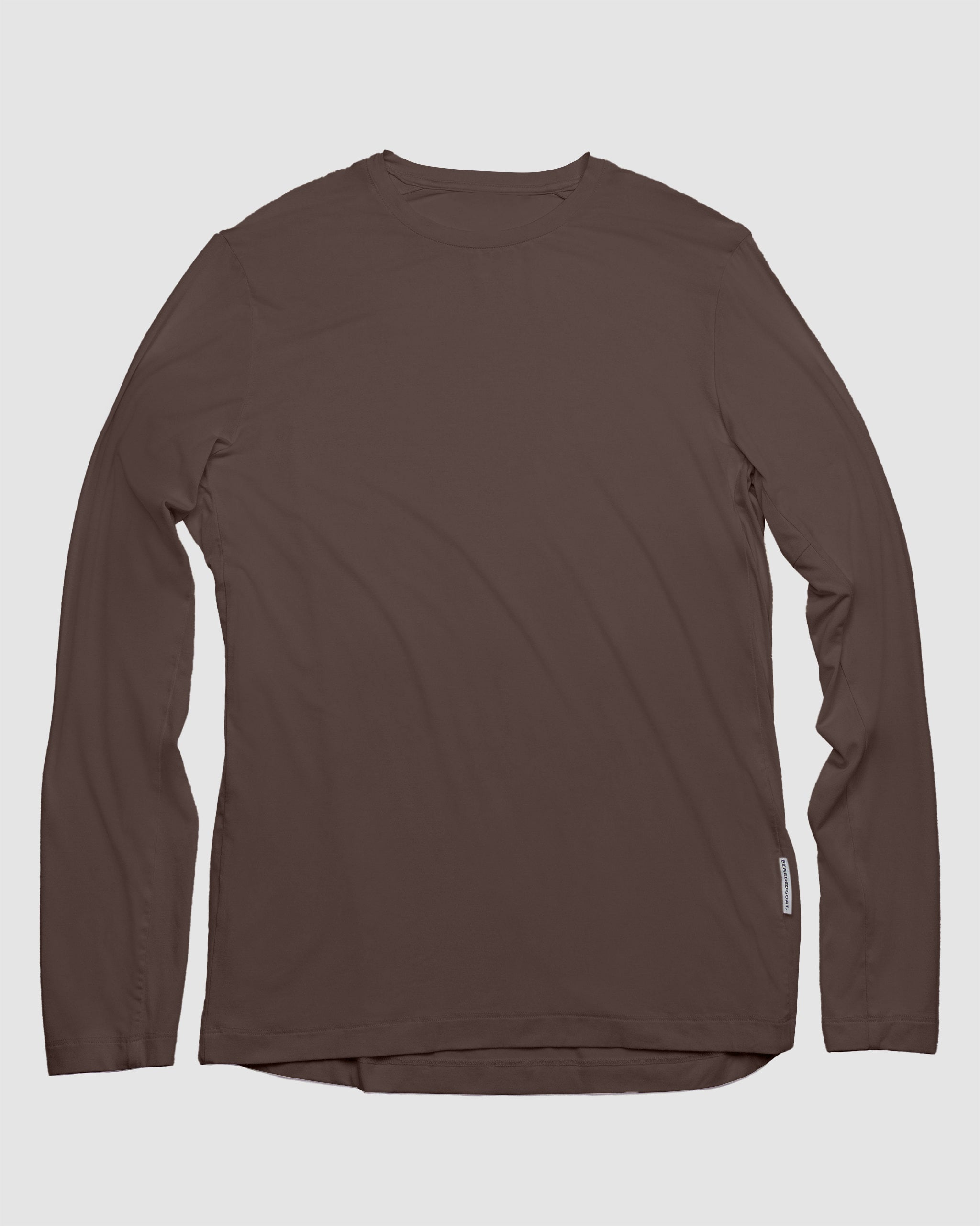 The BEARDEDGOAT Men’s EverZen™ Long Sleeve, shown in Dark Earth, is a versatile crew neck shirt made from a soft bamboo blend. It’s laid flat on a light gray background with a small white tag near the right hem.