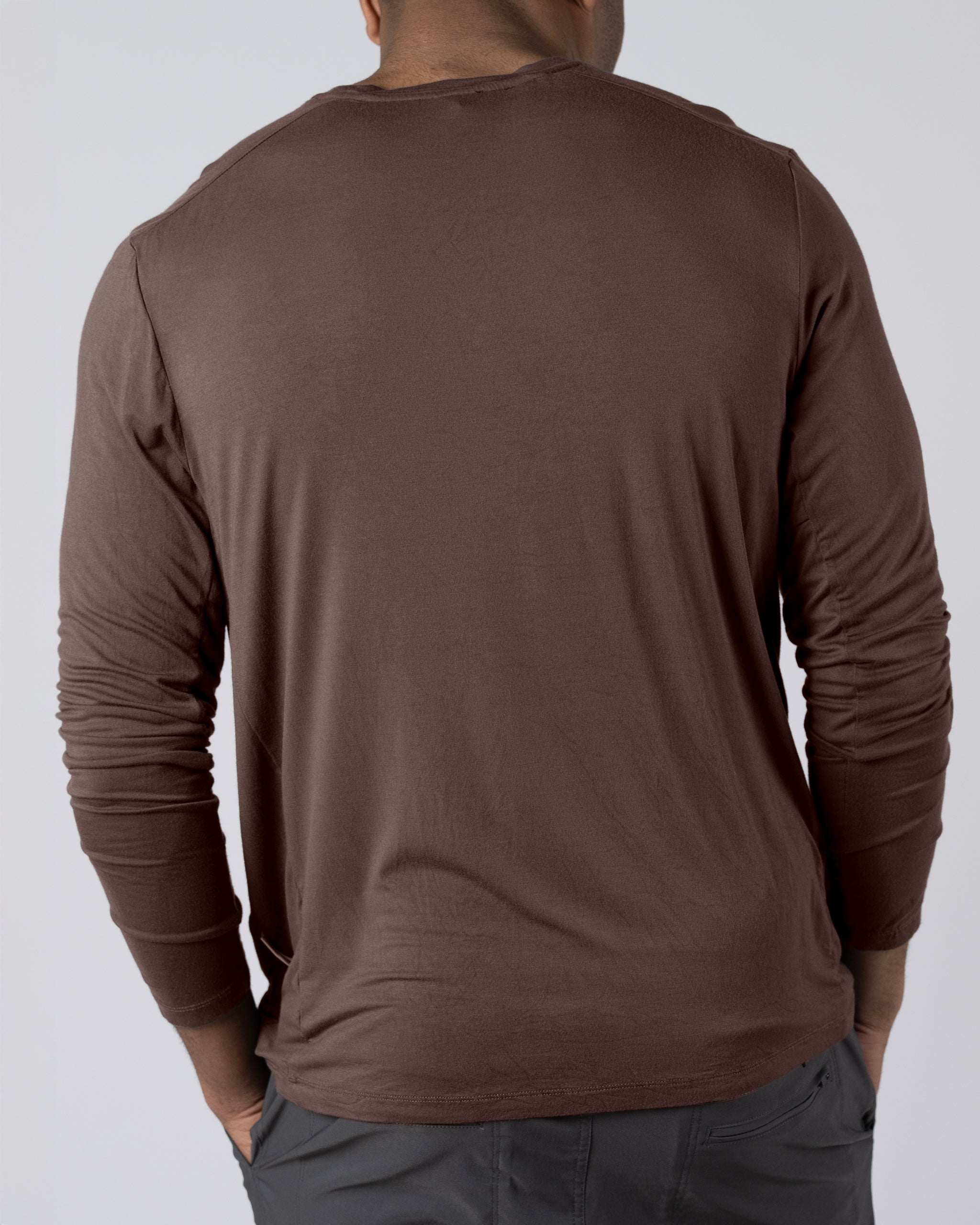 A man seen from behind wears the BEARDEDGOAT Men’s EverZen™ Long Sleeve shirt in brown and gray pants, standing against a plain light background.