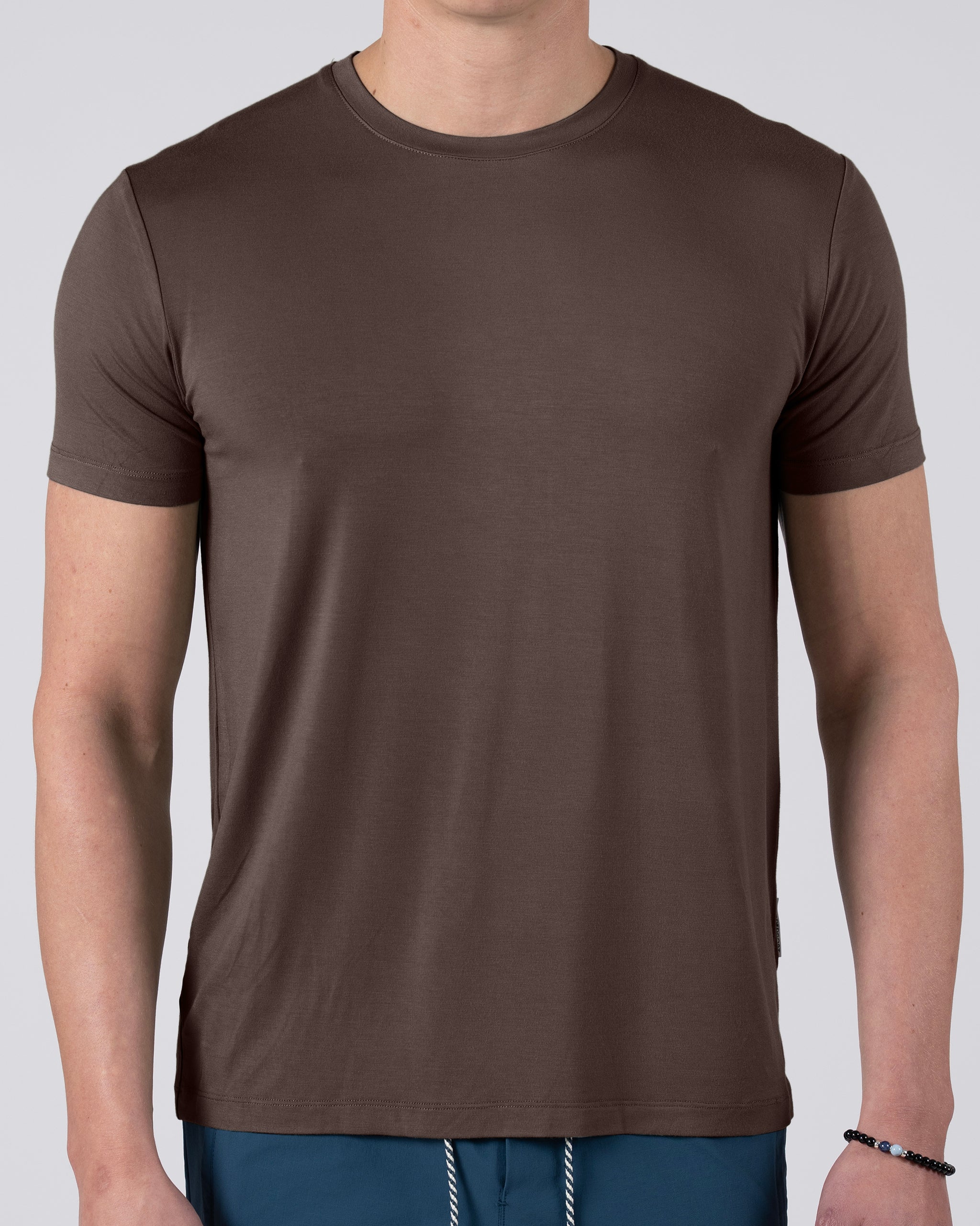 A person wears a BEARDEDGOAT Men’s EverZen™ Short Sleeve bamboo blend crew neck t-shirt in brown with blue pants, standing against a neutral background. Only their upper body is visible; the face is not shown.