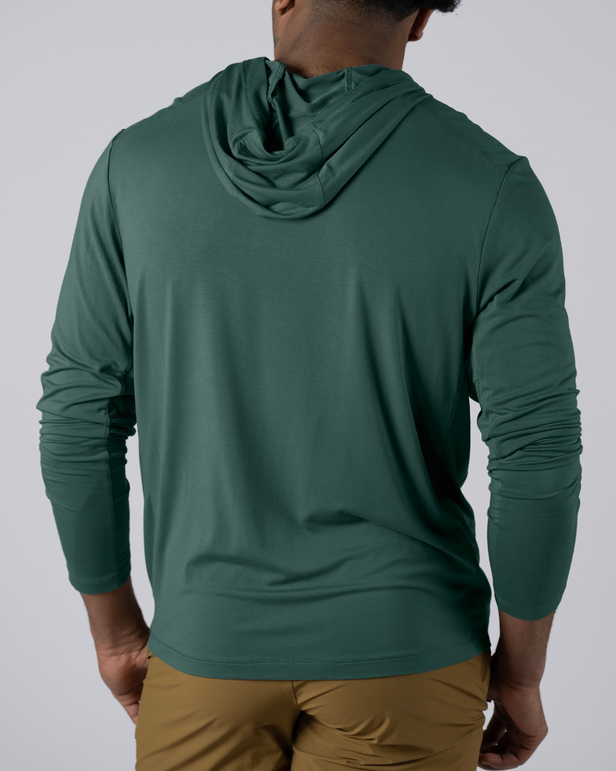 A man wearing a green BEARDEDGOAT Men’s EverZen™ Hoodie and tan pants is shown from the back against a plain light backdrop.
