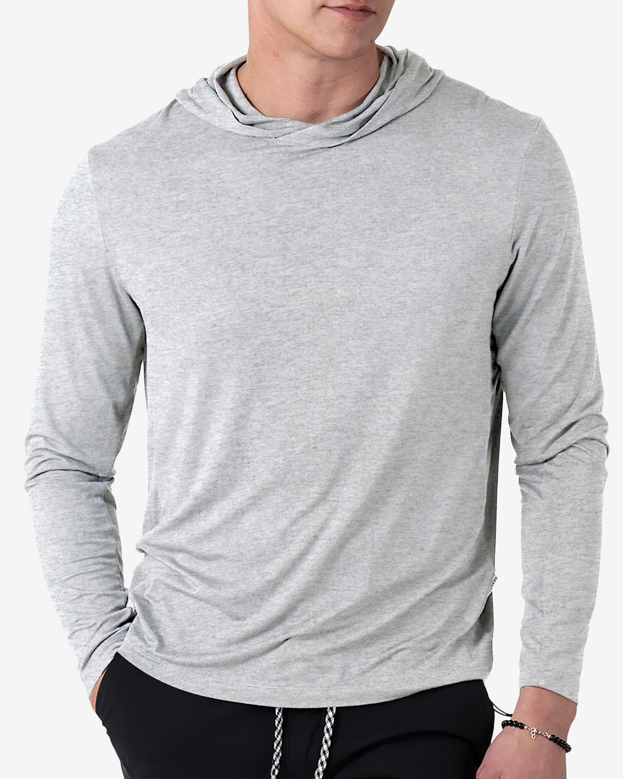 A man wears the BEARDEDGOAT Men’s EverZen™ Hoodie in light gray with black pants, posing with one hand in his pocket against a plain white background—ideal for sustainable clothing enthusiasts.