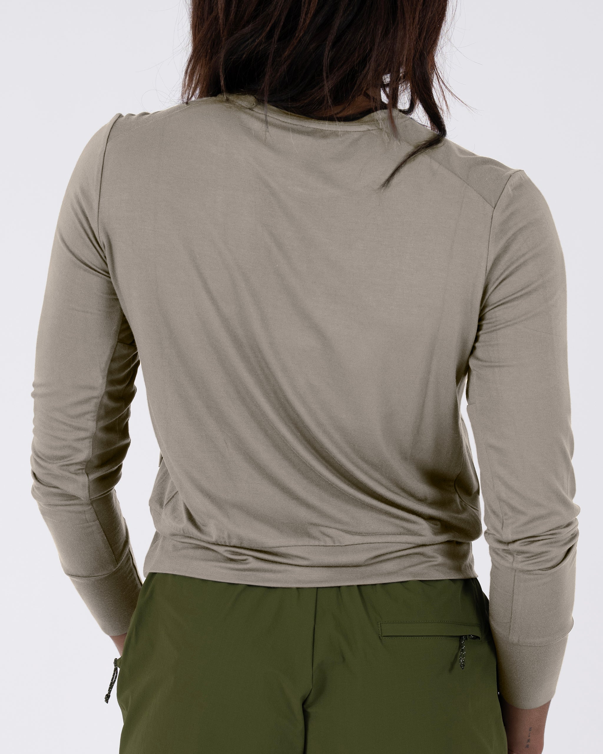 A woman with long dark hair is seen from behind wearing a BEARDEDGOAT Women’s EverZen™ Bamboo Long Sleeve in light gray and olive green pants, set against a plain white background.