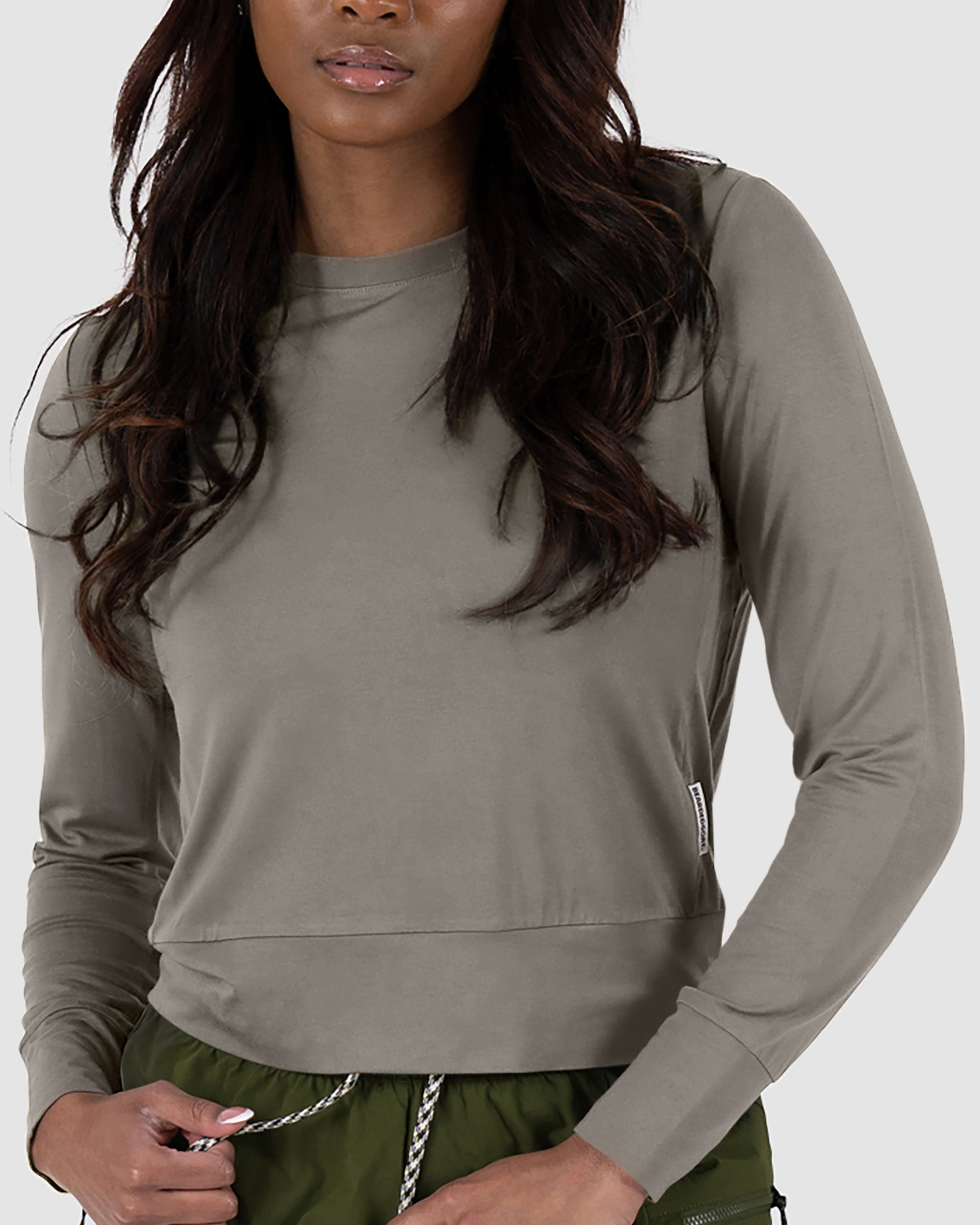 A woman wears the BEARDEDGOAT Women’s EverZen™ Bamboo Long Sleeve in Terra Sienna, standing against a plain light background.