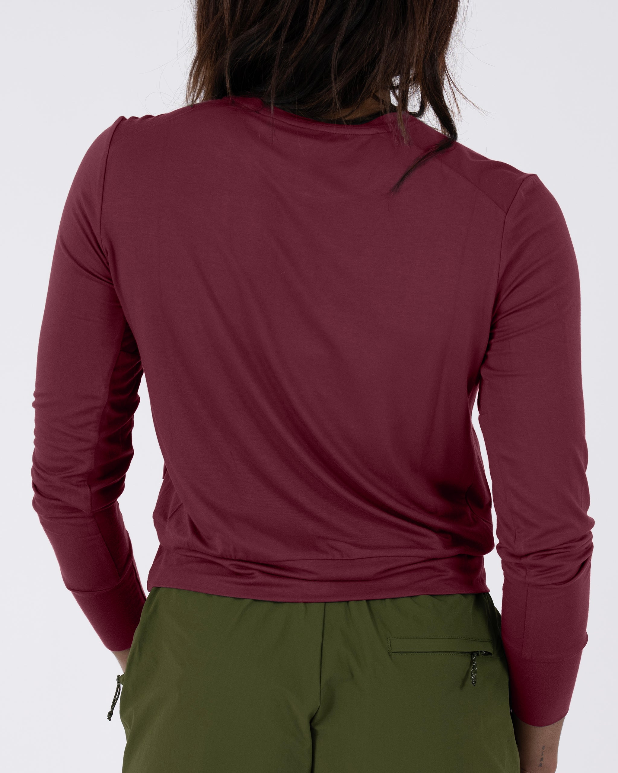 A person with long dark hair wears the BEARDEDGOAT Women’s EverZen™ Bamboo Long Sleeve in maroon, paired with olive green pants, shown from the back against a plain white background.