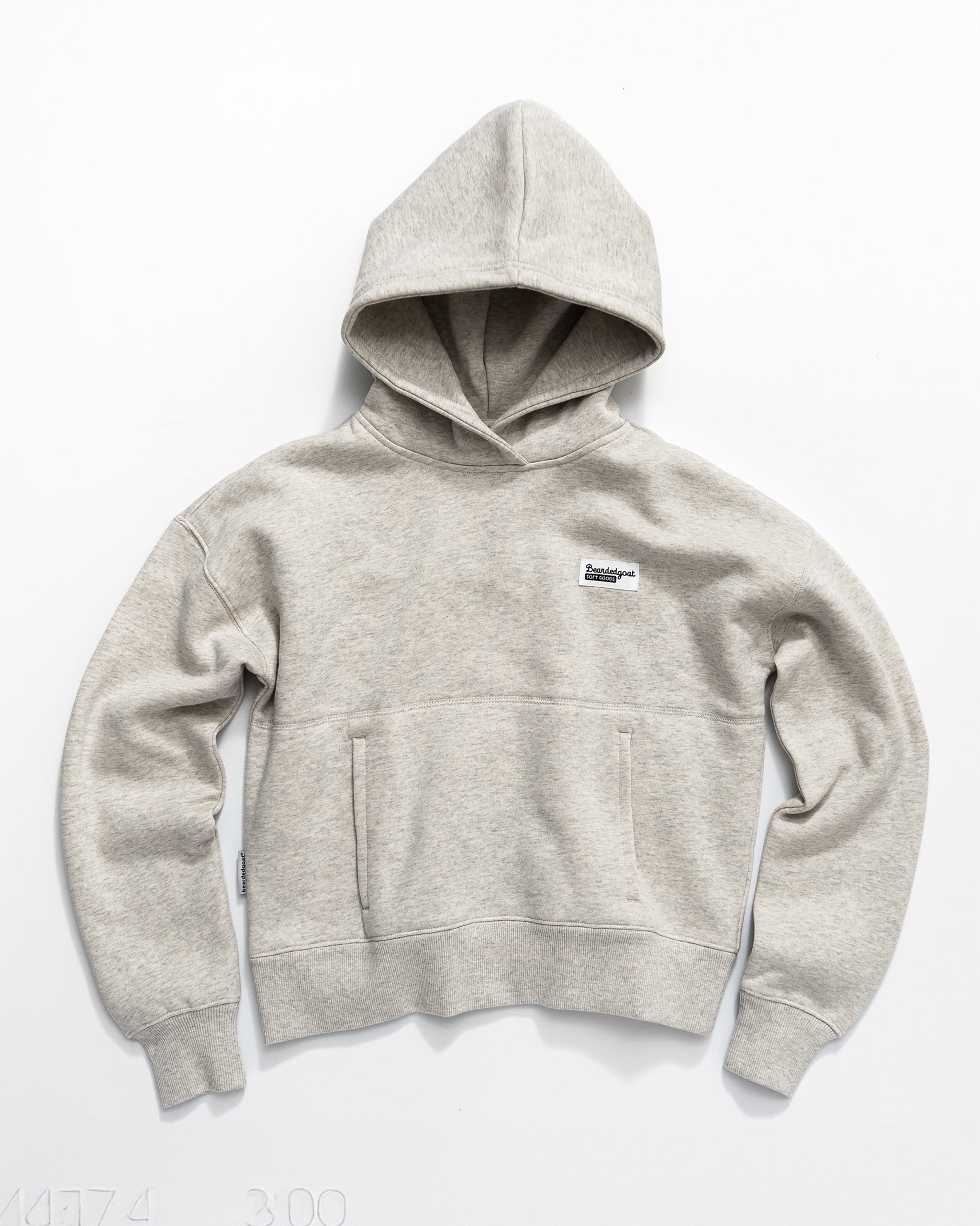 The Women's Overnight Hoodie by beardedgoat is a light gray, long-sleeve sweatshirt with a front pocket and a small rectangular patch on the left chest, shown laid flat on a white surface.