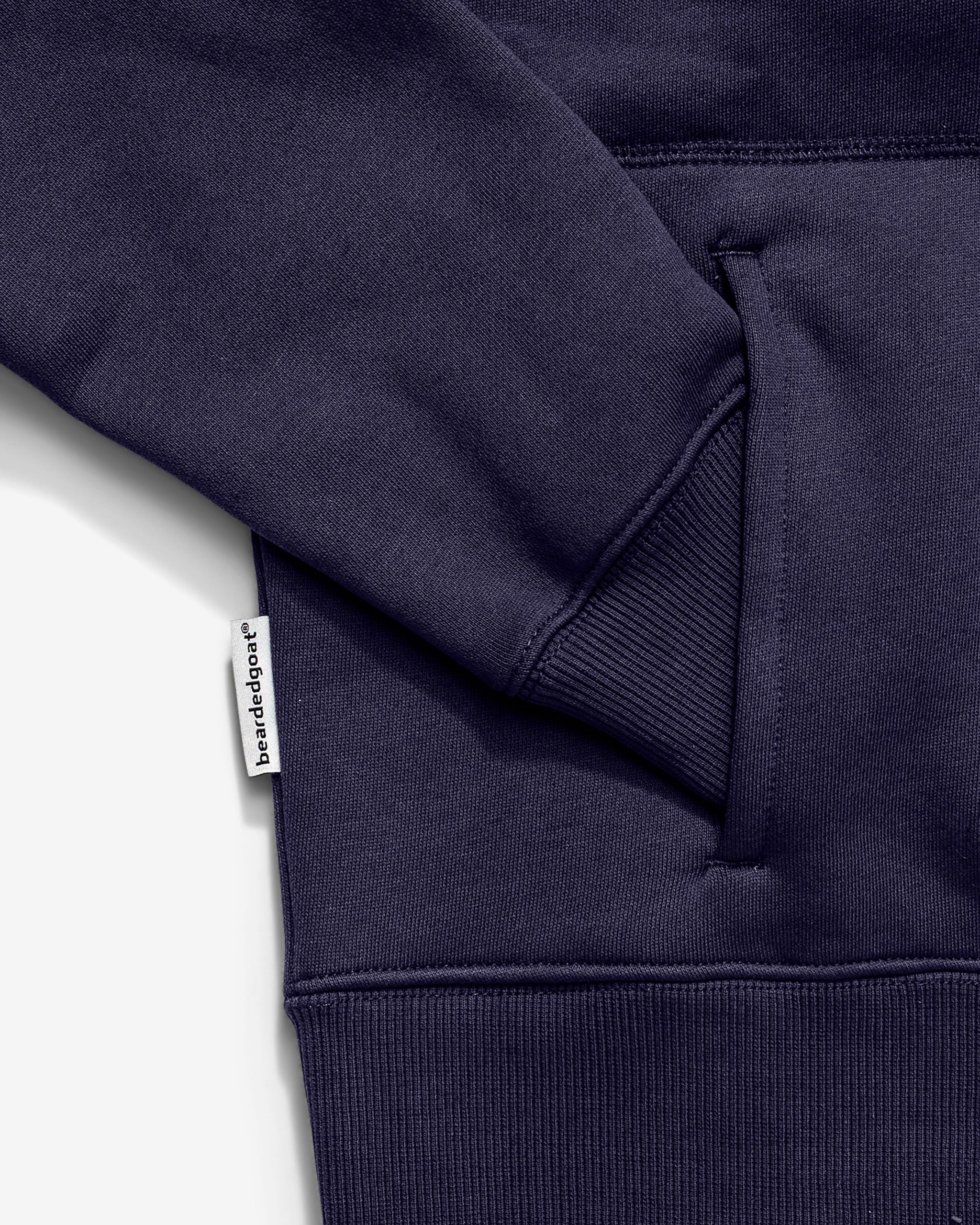 A close-up of the Women's Overnight™ Hoodie by beardedgoat in navy blue cotton fleece, showing the pocket and sleeve with a small white bare & edge tag on the side seam near the pocket.