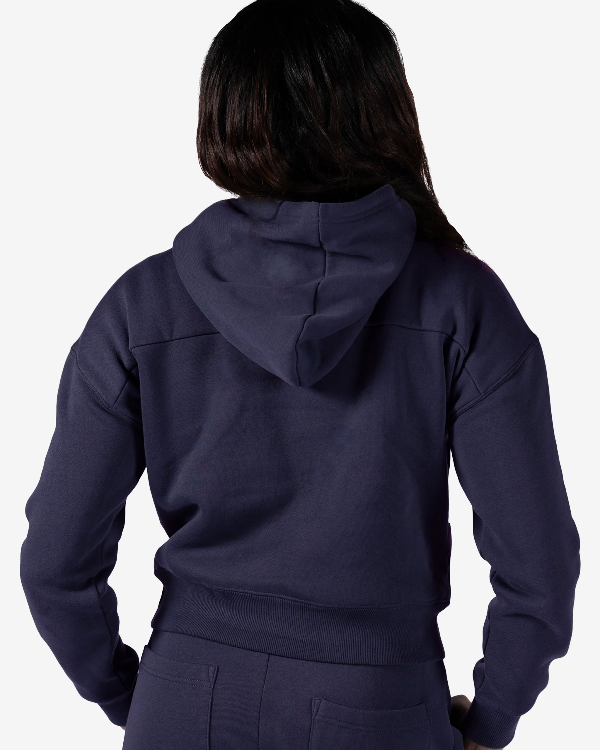 A woman with long dark hair is shown from behind wearing the beardedgoat Women's Overnight™ Hoodie and matching pants, standing against a plain white background.