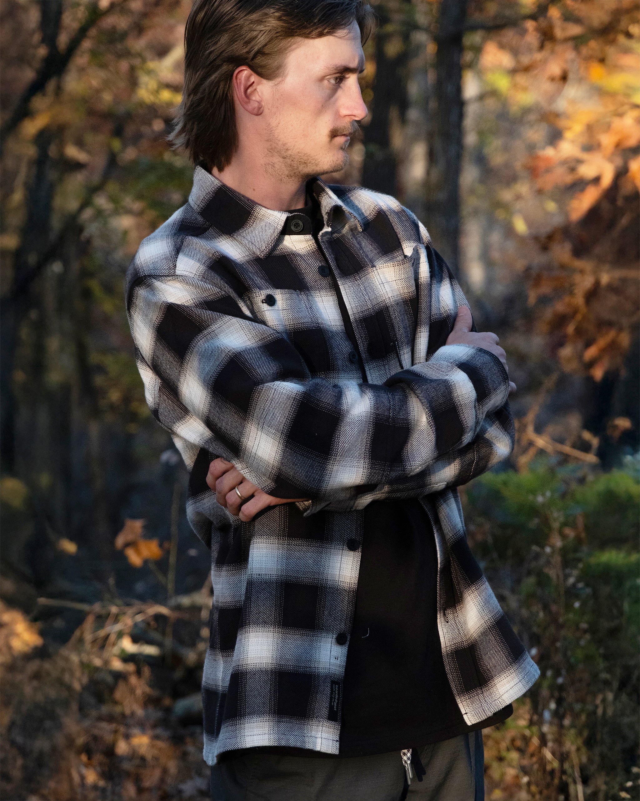 A man with light brown hair and a mustache stands outside among autumn leaves, arms crossed, wearing the NEW--Ozark Utility Flannel™ shirt by beardedgoat.