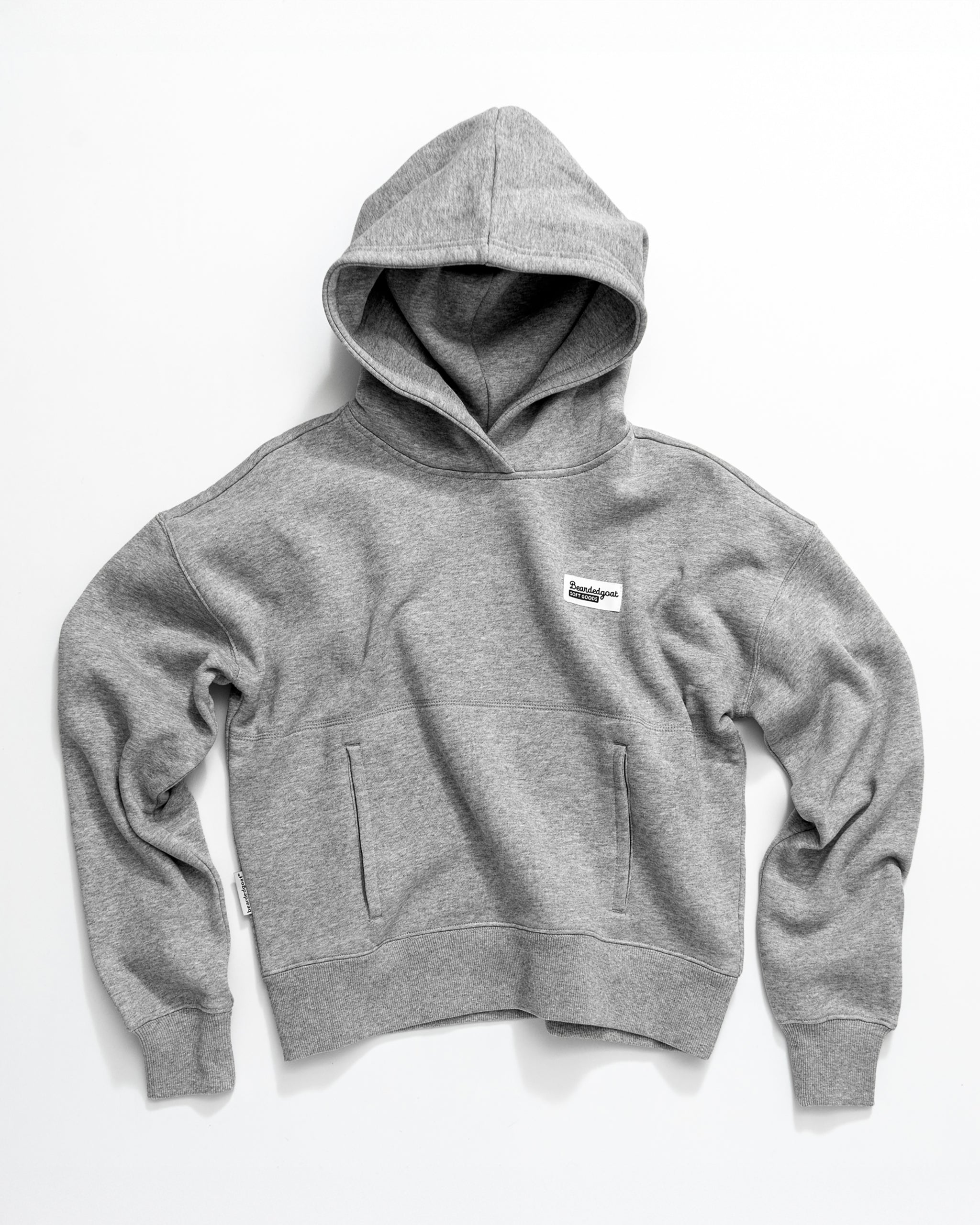 The beardedgoat Women's Overnight Hoodie in heather gray is made from heavyweight cotton fleece, featuring a front kangaroo pocket and a small white rectangular chest patch, shown flat on a white background.