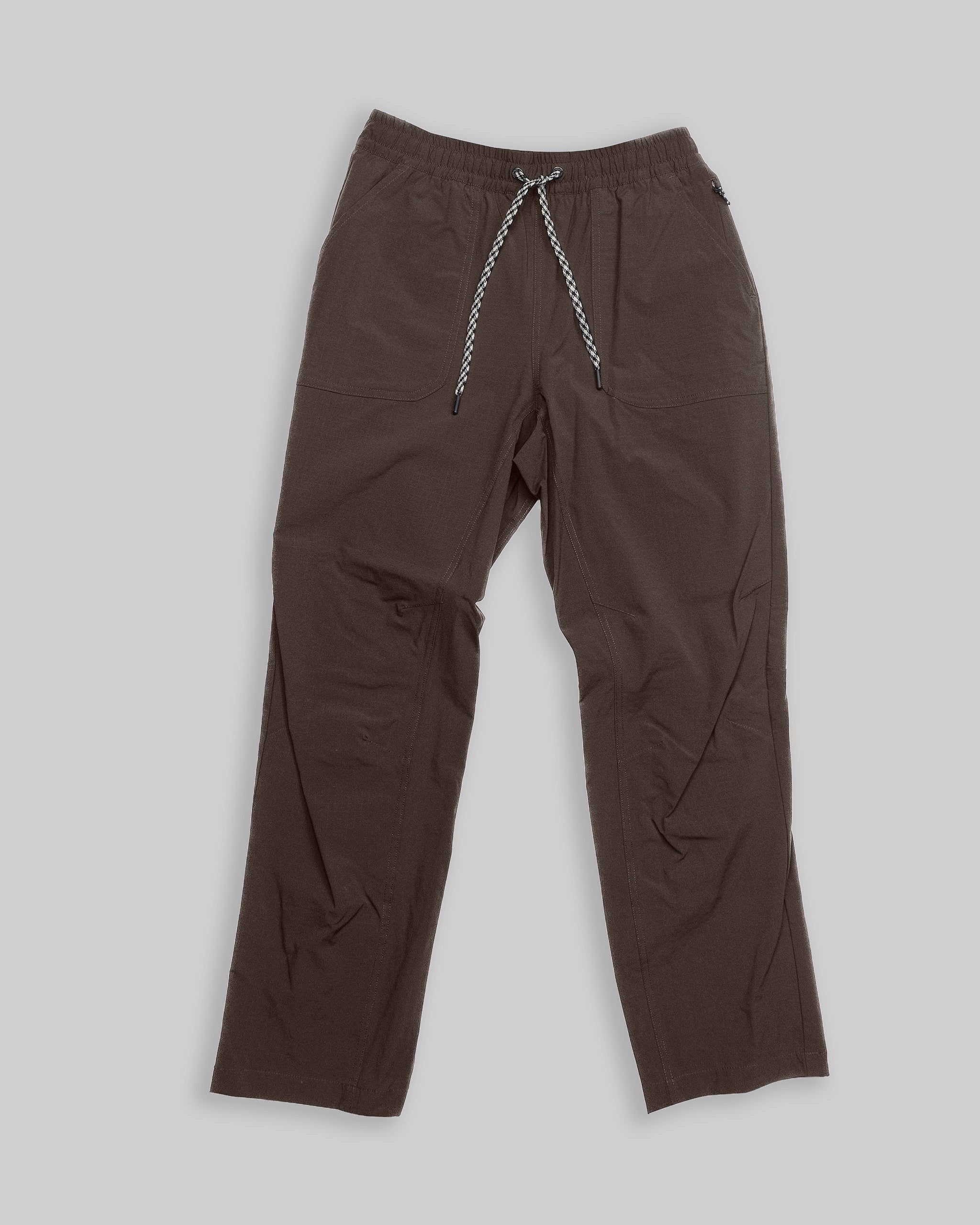 The BEARDEDGOAT NEW — Summit™ Pant is a loose-fitting brown women’s performance pant with an elastic waistband and black-and-white drawstring, made from durable stretch fabric and shown flat on a light gray background.