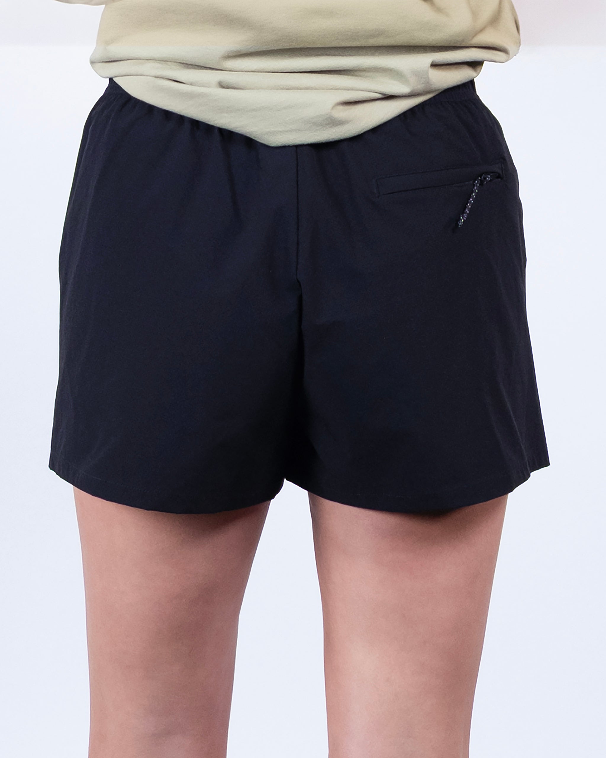 A person wears BEARDEDGOAT Summit Short trail shorts, crafted from lightweight ripstop fabric with a small zippered back right pocket, standing against a plain white background.