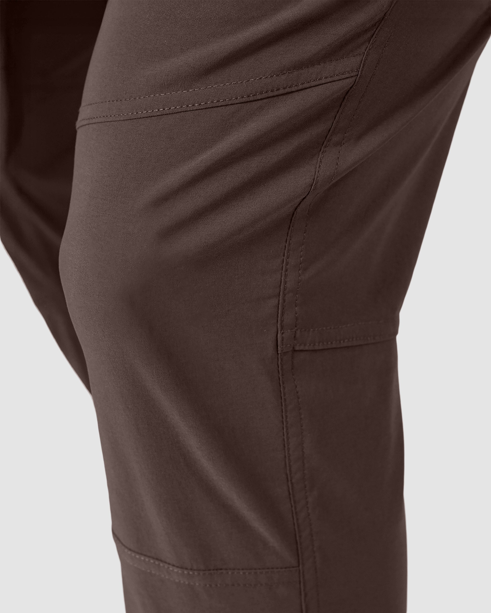 Close-up of a person wearing BEARDEDGOAT NEW—ROVER™ Pant in brown, highlighting the side seam, pocket outline, and detailed stitching against a light gray background.