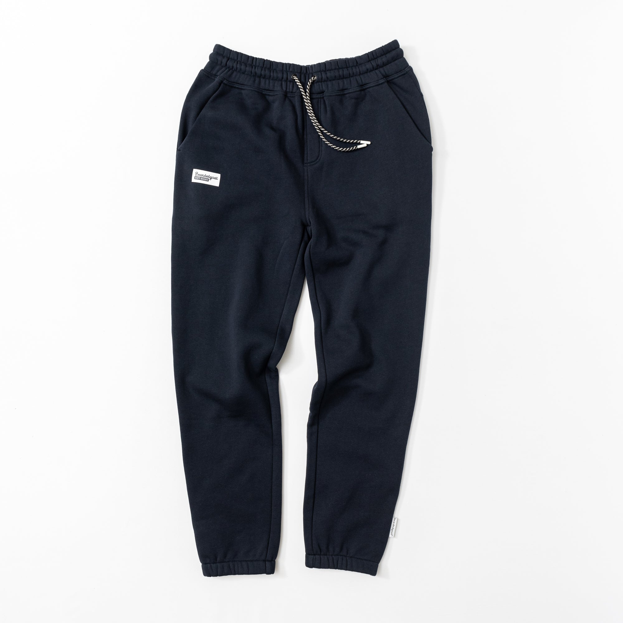 The BEARDEDGOAT Women’s Overnight™ Classic Jogger in dark navy features a high-rise waistband, white drawstring, front pockets, elastic cuffs, and a small white patch. Made from heavyweight cotton fleece for comfort all day.
