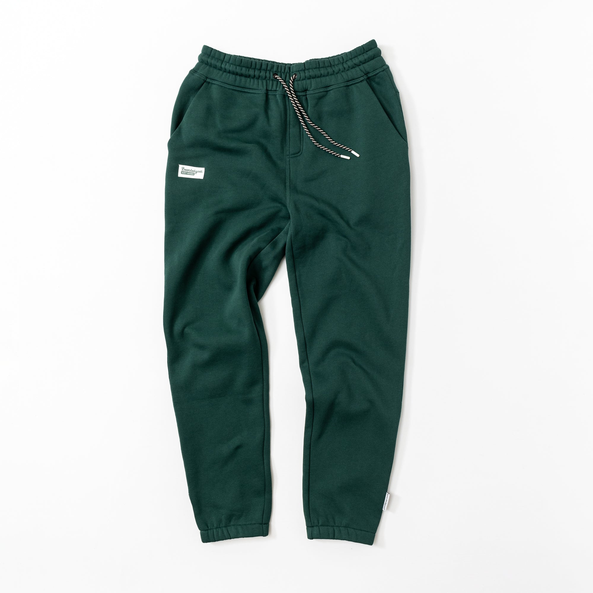 The BEARDEDGOAT Women’s Overnight™ Classic Jogger in Forest features a high-rise waistband, black-and-white drawstring, side pockets, and a small white patch on the left thigh. Made from heavyweight cotton fleece, shown laid flat on a white background.