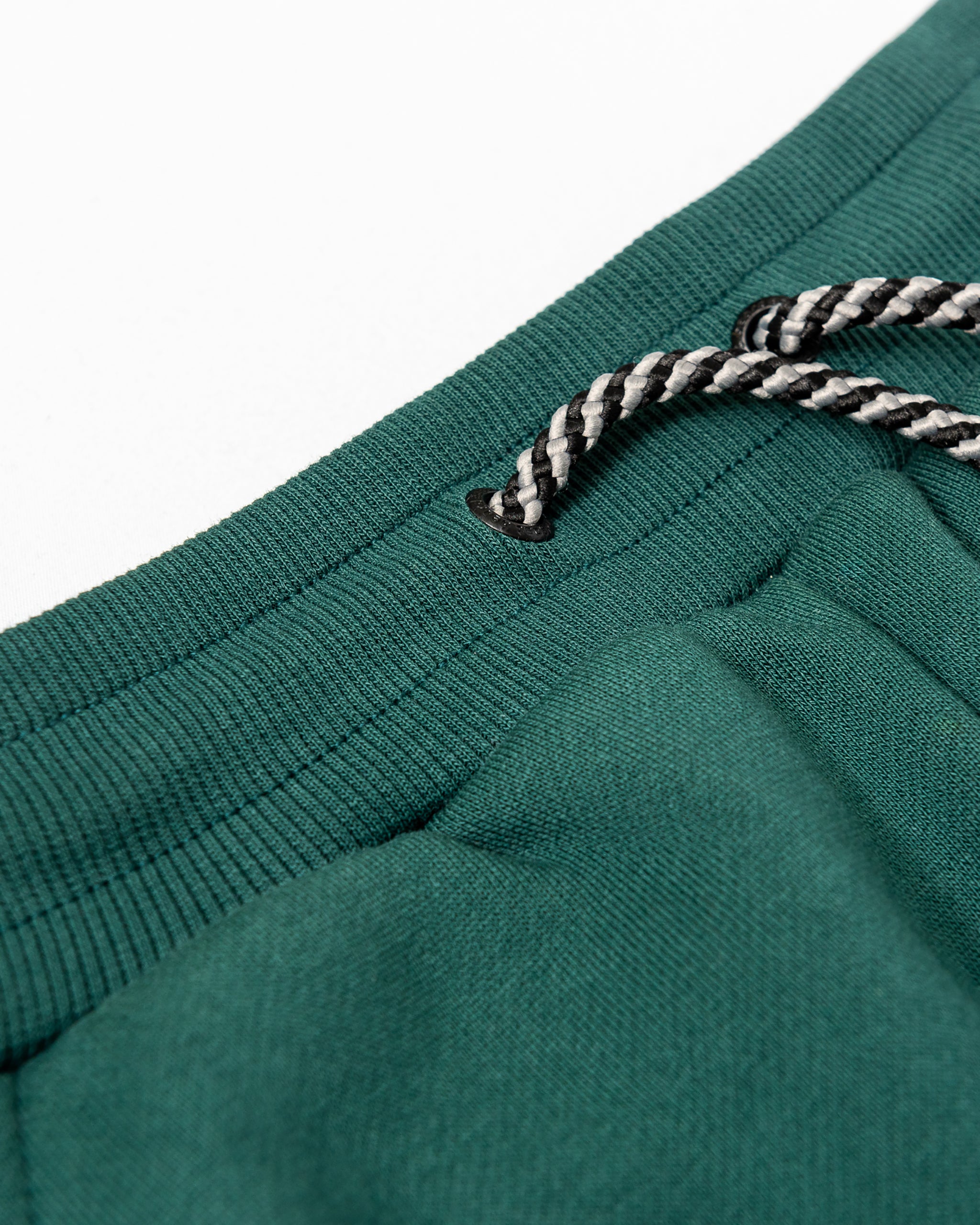 Close-up of the beardedgoat Women’s Overnight Sweatpant in green heavyweight cotton fleece shows a ribbed waistband with black-and-white braided drawstrings threaded through metal eyelets.