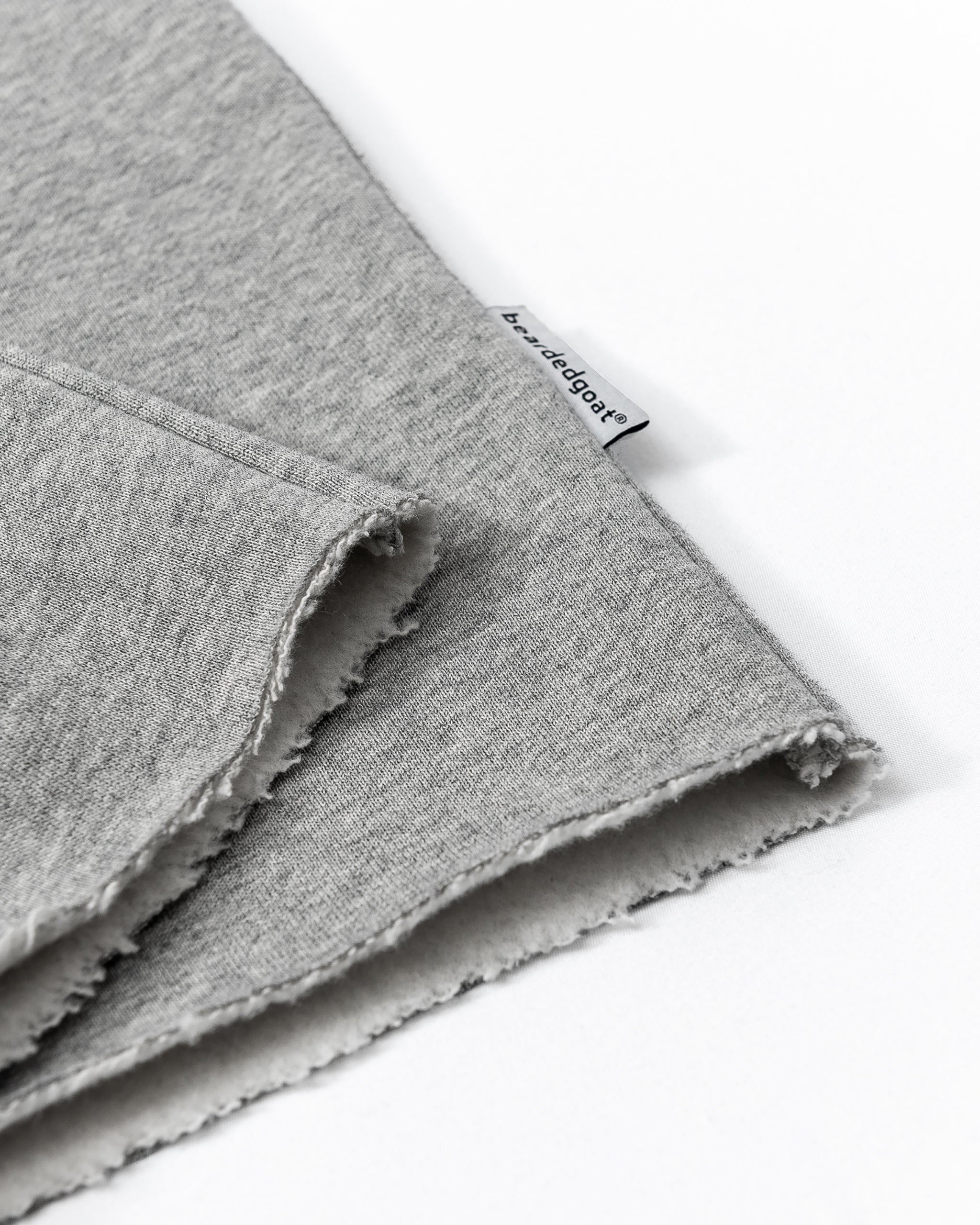Close-up of two overlapping pieces of light gray heavyweight cotton fleece with raw edges and a small white beardedgoat tag. Perfect for designing the Women’s Overnight Sweatpant, ideal for comfortable loungewear.
