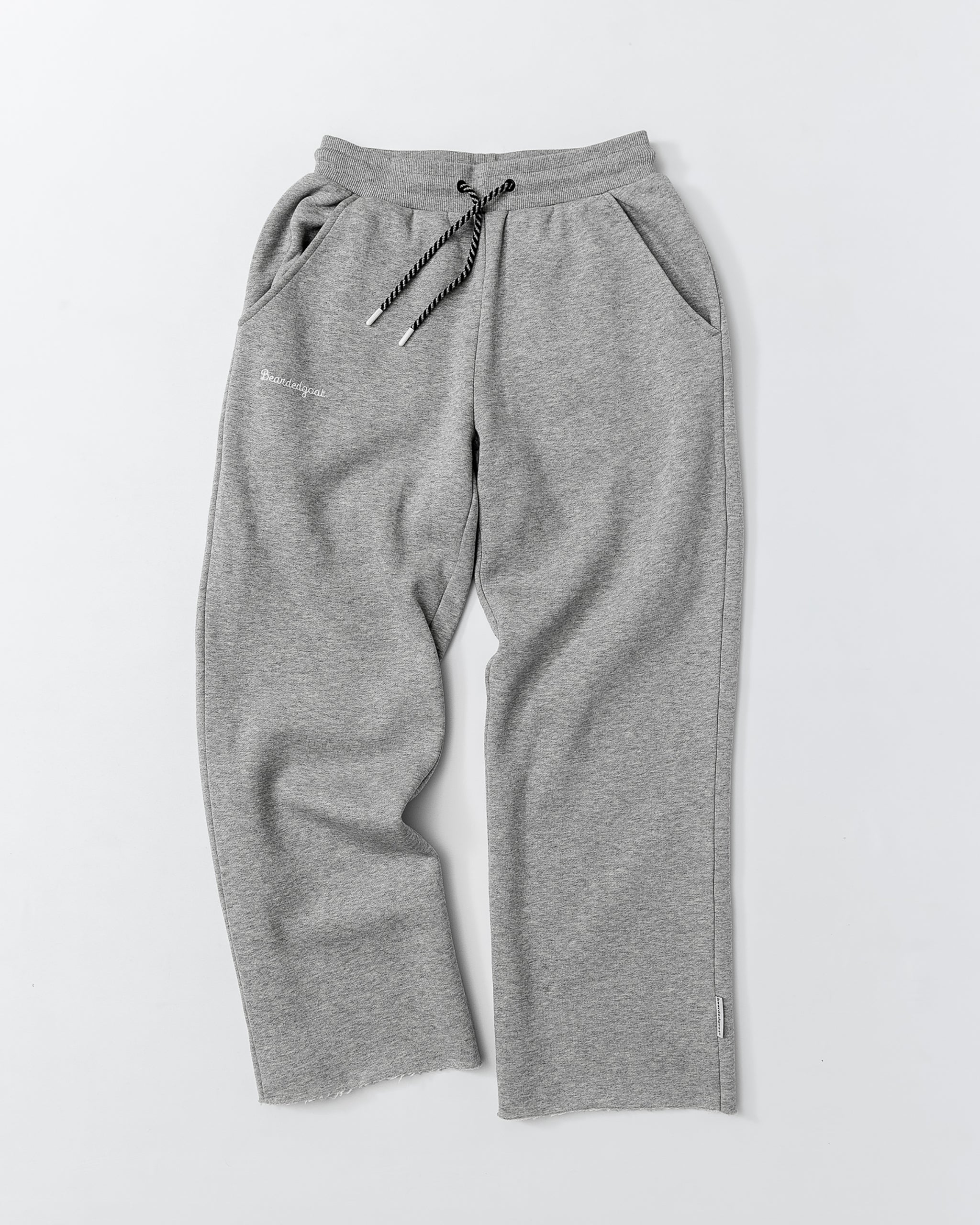 The beardedgoat Women’s Overnight Sweatpant is a light gray heavyweight cotton fleece pant with black and white drawstring, side pockets, and subtle branding on the left pocket, shown laid flat on a white background.