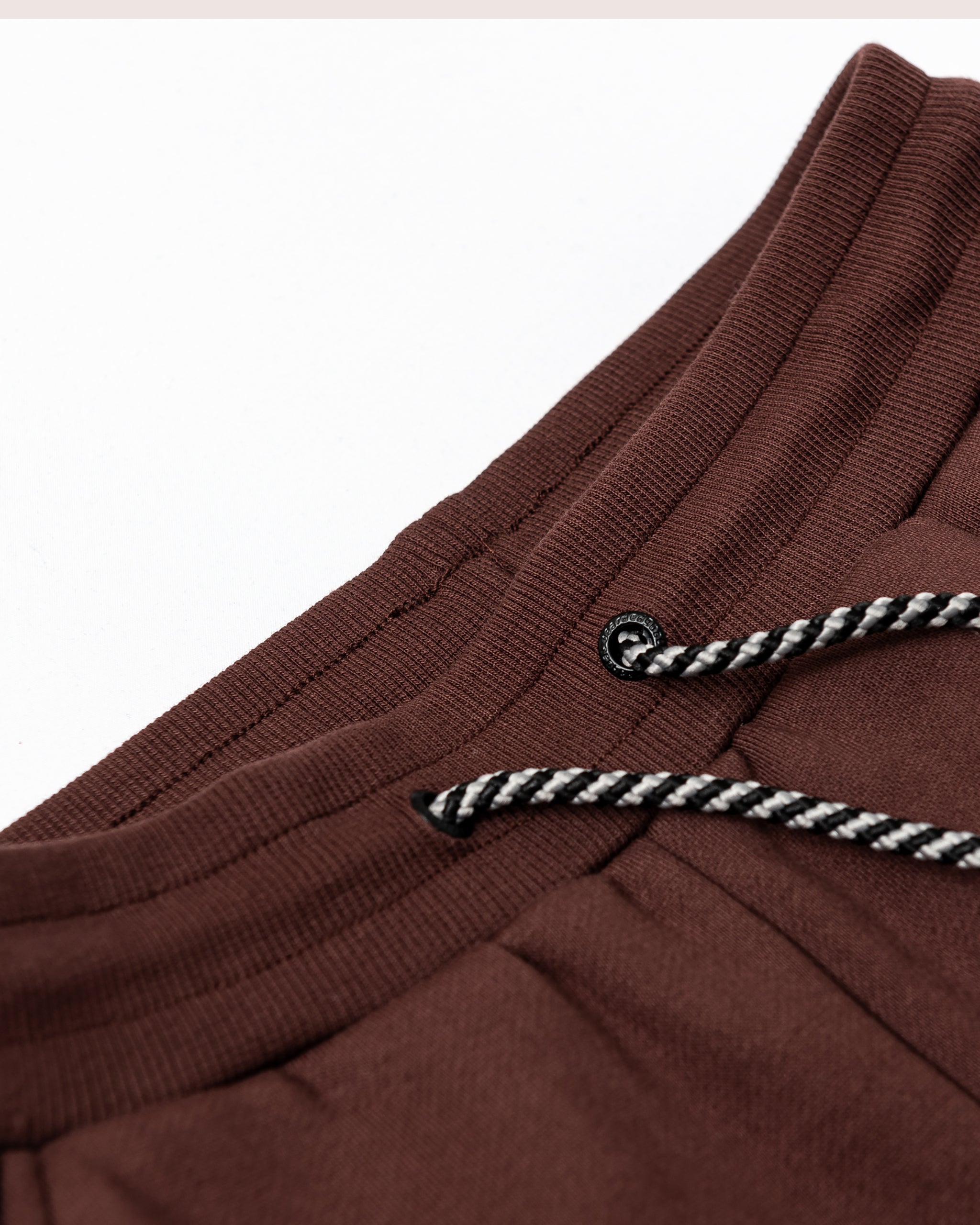 Close-up of the waistband of beardedgoat Women’s Overnight Sweatpant in brown heavyweight cotton fleece with black and white striped drawstrings, shown on a white surface.