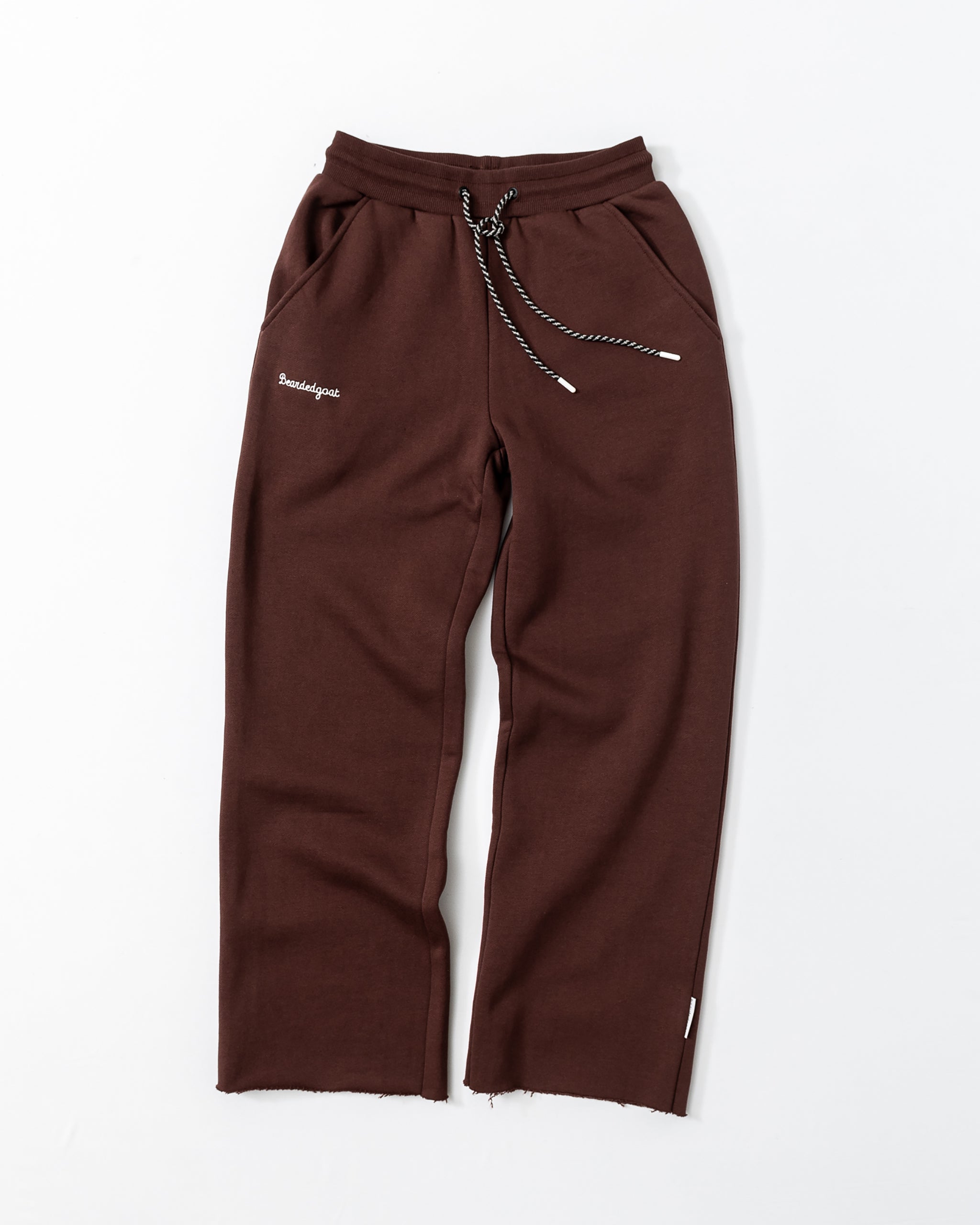 The beardedgoat Women’s Overnight Sweatpant in brown is made from heavyweight cotton fleece, features a drawstring waist, side pockets, white "Bonjour" embroidery, relaxed fit, and raw hems—ideal comfy loungewear.
